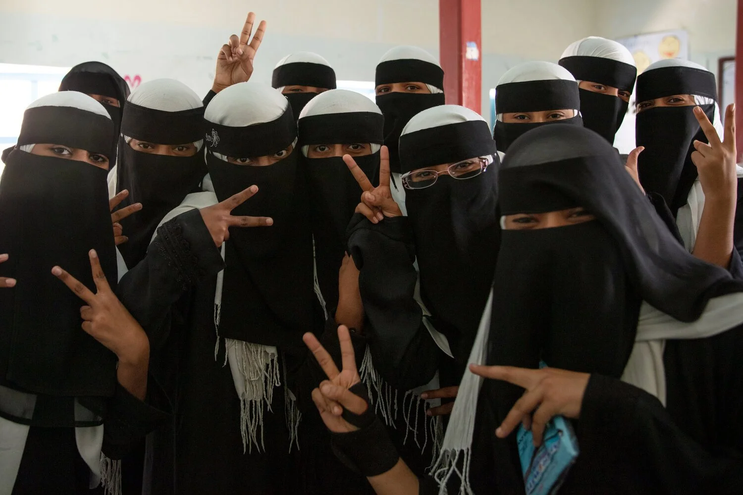 Teenage girls pose for a photo at the Girls School in the village of Sif in central Yemen’s Hadhramaut region. After reaching puberty, girls’ school uniforms include a black abaya, white hijab and black niqab.   Photo by Nicole Smoot.
