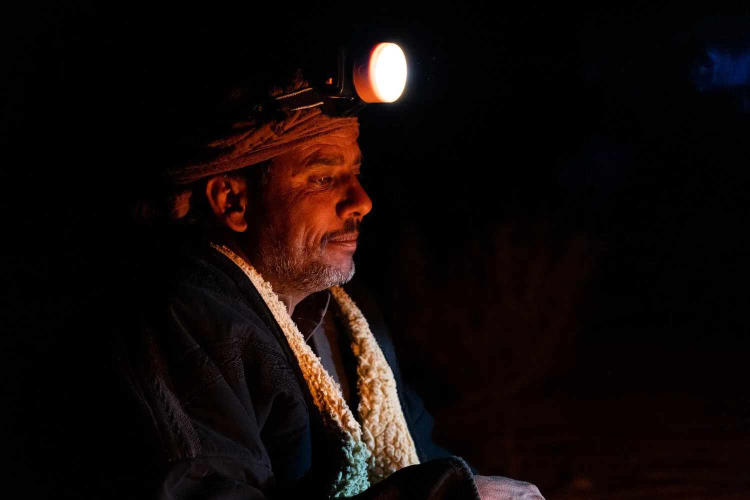 A portrait of a Mahri bedouin man with a headlamp sitting around the fire in the Empty Quarter Desert. Yemen.