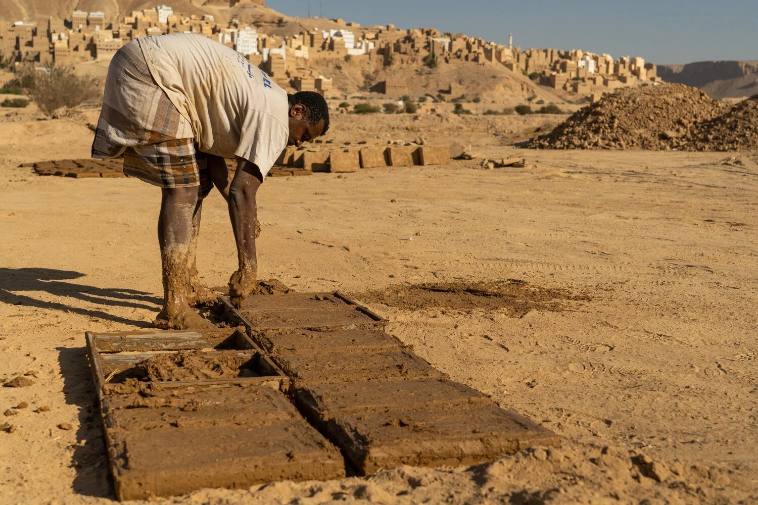 A Yemeni man making mud bricks in the sun.