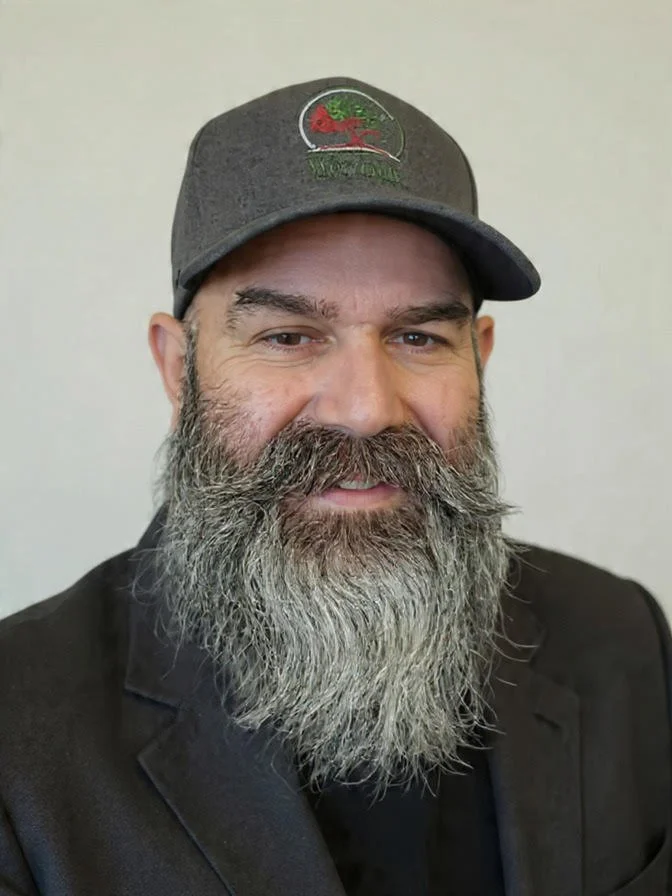 A man with a gray beard and wearing a gray baseball cap with a red and green logo, smiling at the camera against a plain background. woodside health insurance in Wisconsin helping business find affordable health insurance
