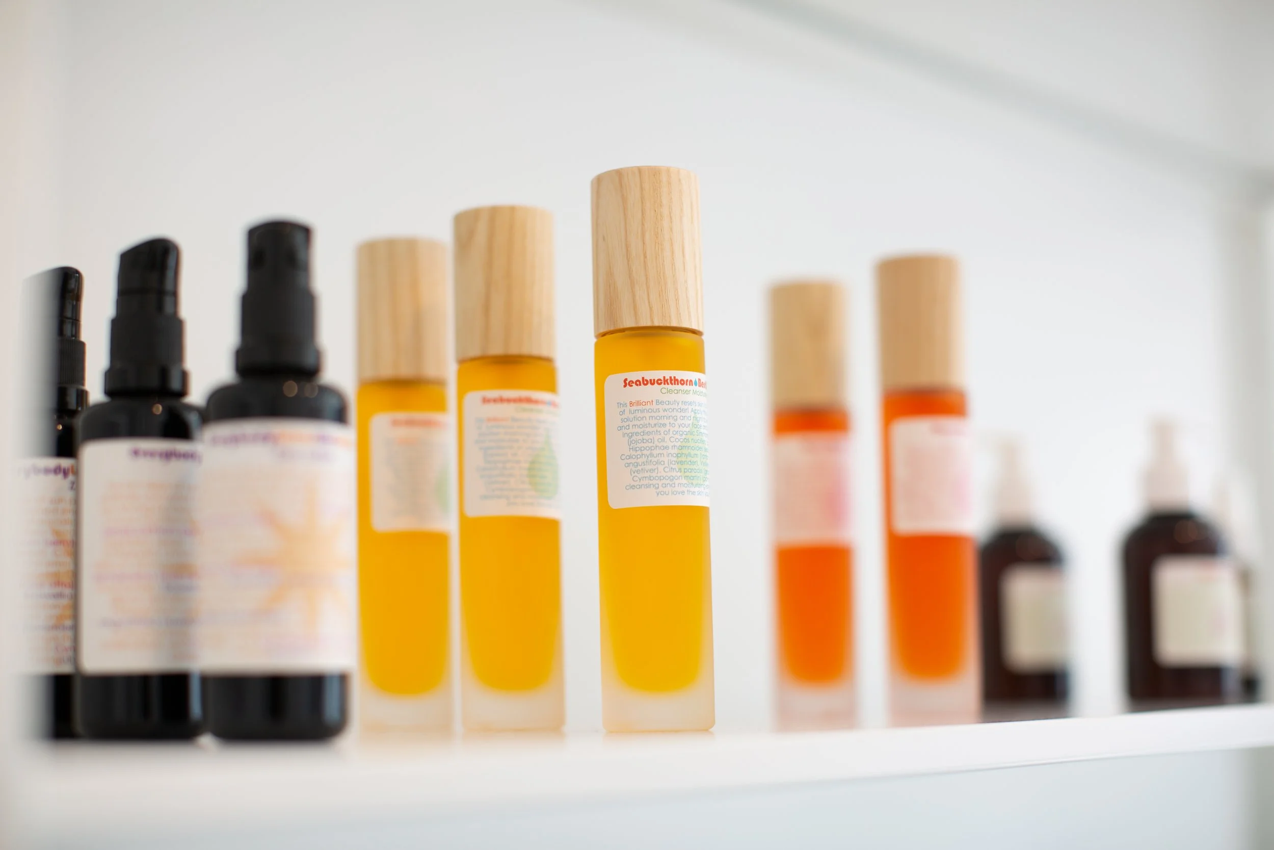 Row of Living Libations skincare bottles on a white shelf, with labels and wooden caps visible.