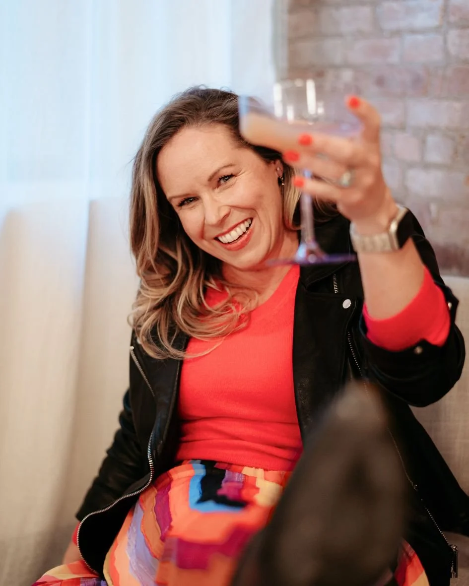 District Band Bar's Kristin Lawton in pink top and leather jacket cheers-ing to the camera with a cockatil