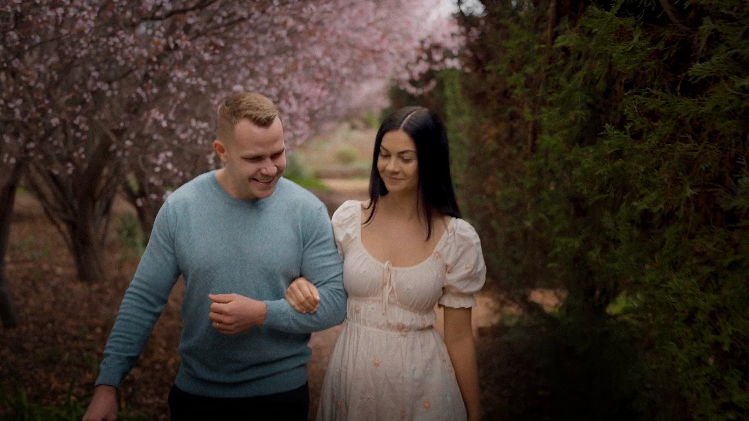 A couple walking through a park with blooming cherry blossom trees.
