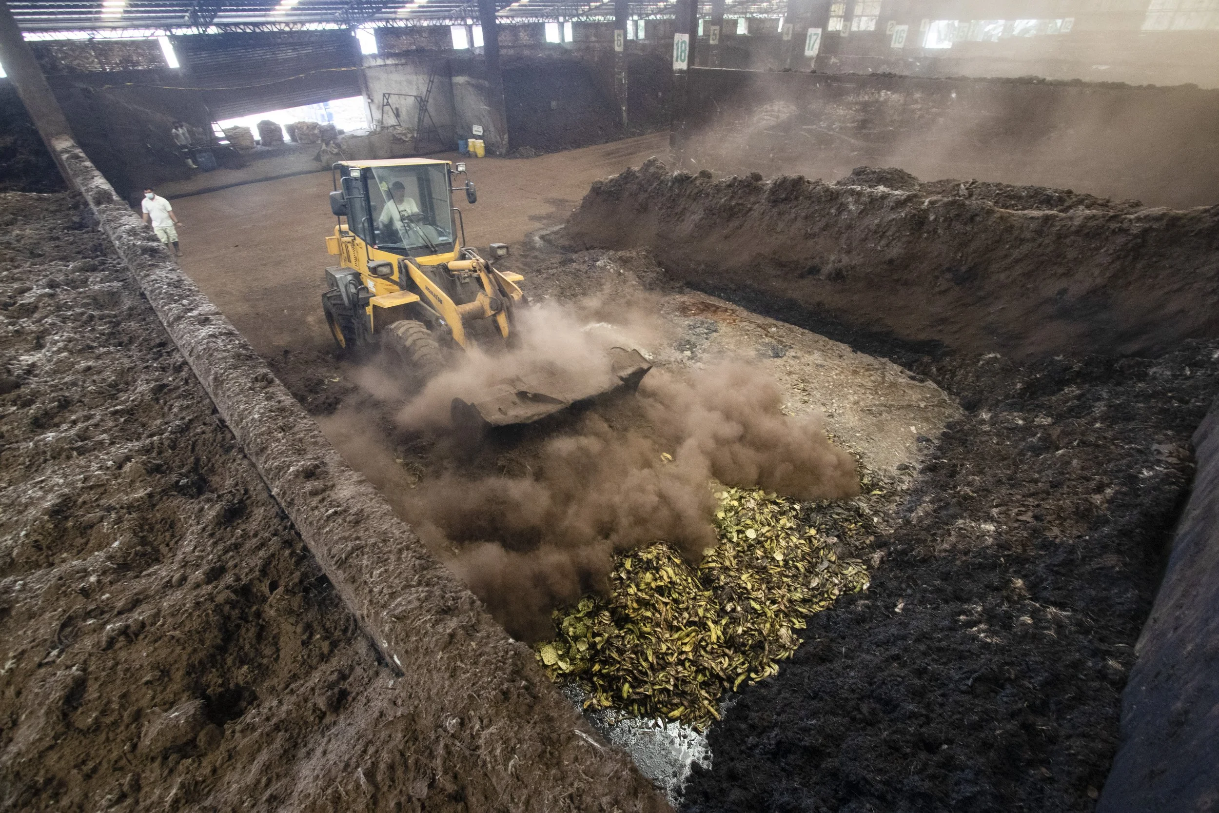 A payloader turns the compost. Smoke rises due to the hot temperature from the active bacteria decomposing the biodegradables.