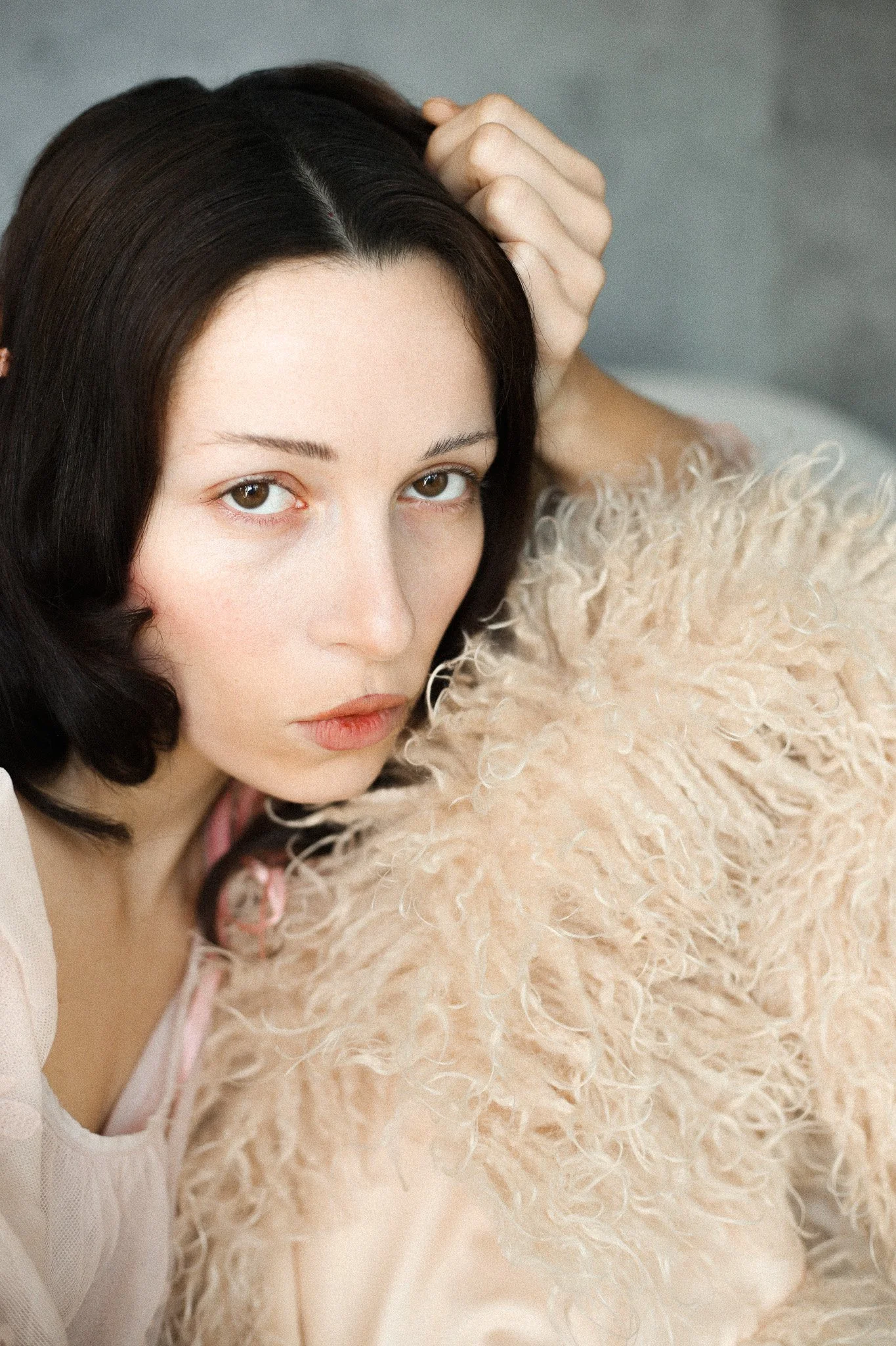 Jeune femme aux cheveux noir, regardant l'objectif, portant un vêtement beige avec un détail en peluche