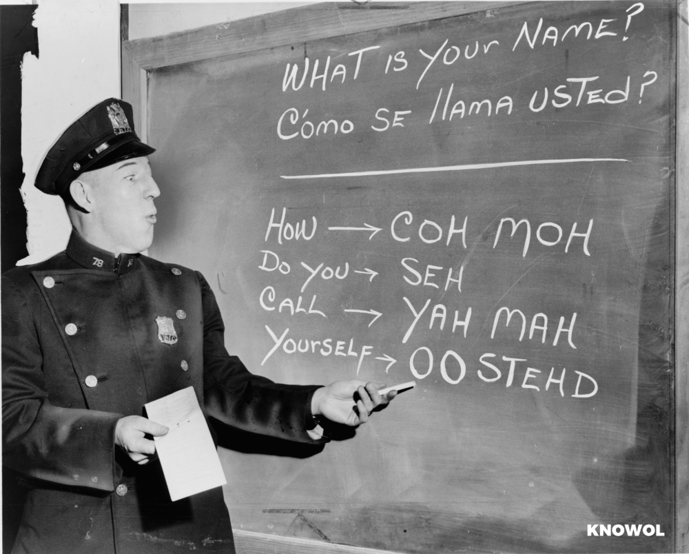 Officer Richard Perry practices basic Spanish phrases using phonetic syllables written on a blackboard, 1958 ©Knowol
