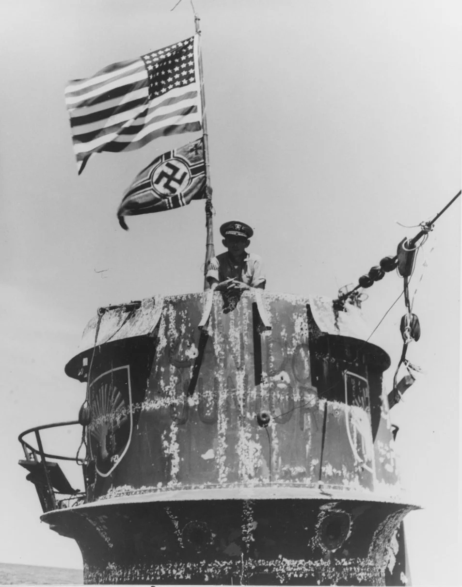 U-505 after capture, showing her scallop shell emblem and a large U.S. flag flying over the German naval ensign.