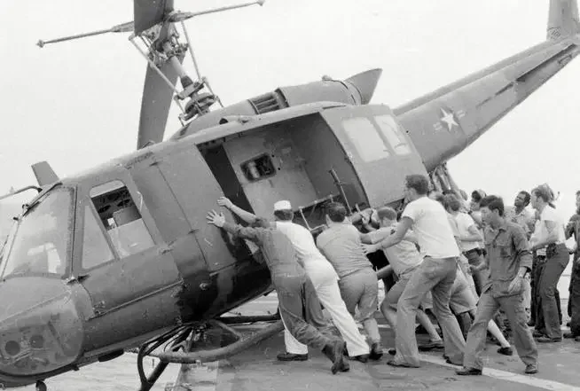KIRK crewmen push a Huey helicopter into the ocean to make room for more crafts carrying refugees, April 1975.