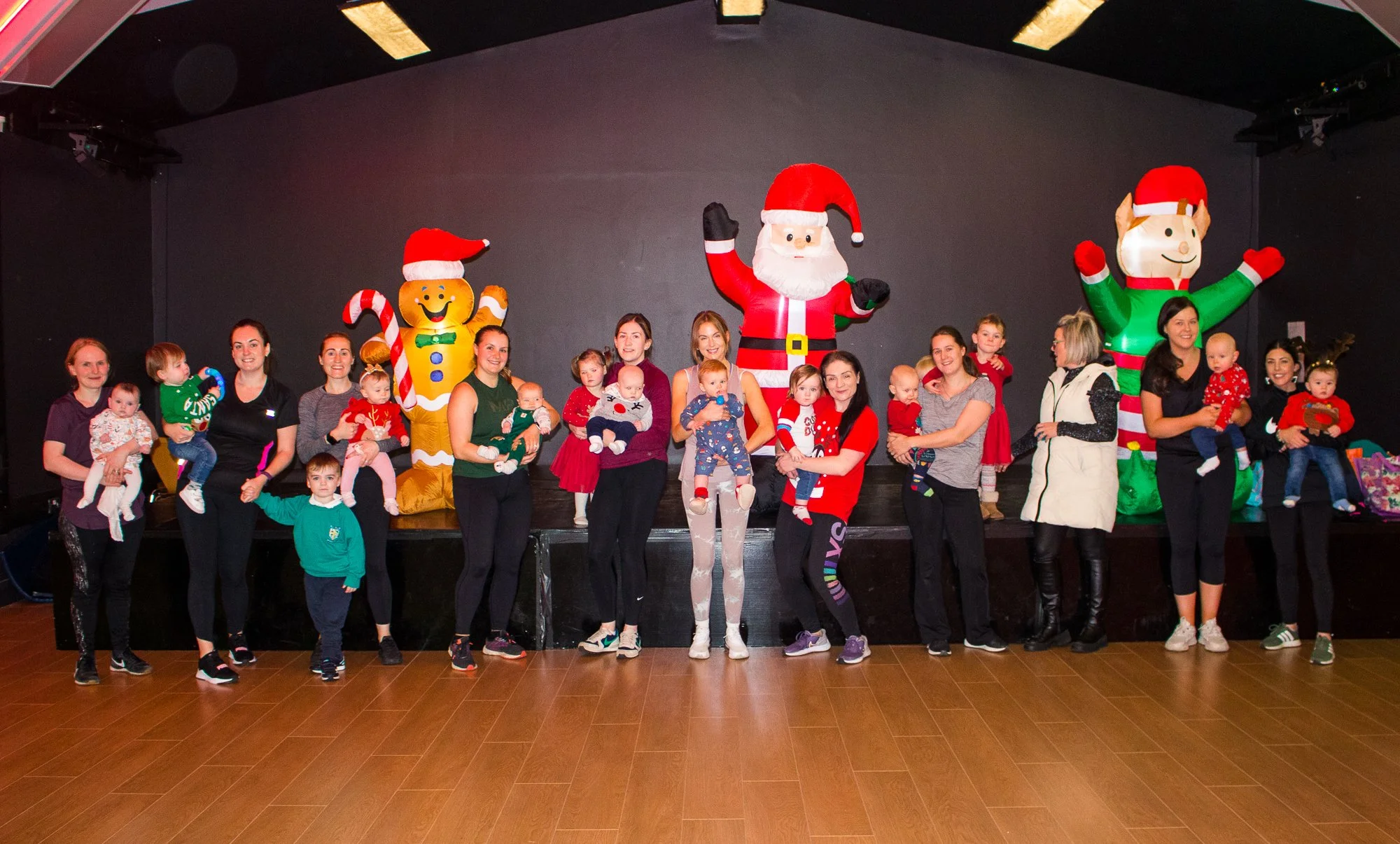 Group of women and children posing in front of Christmas inflatables on a stage. Inflatable characters include Santa Claus, a gingerbread man, and an elf.