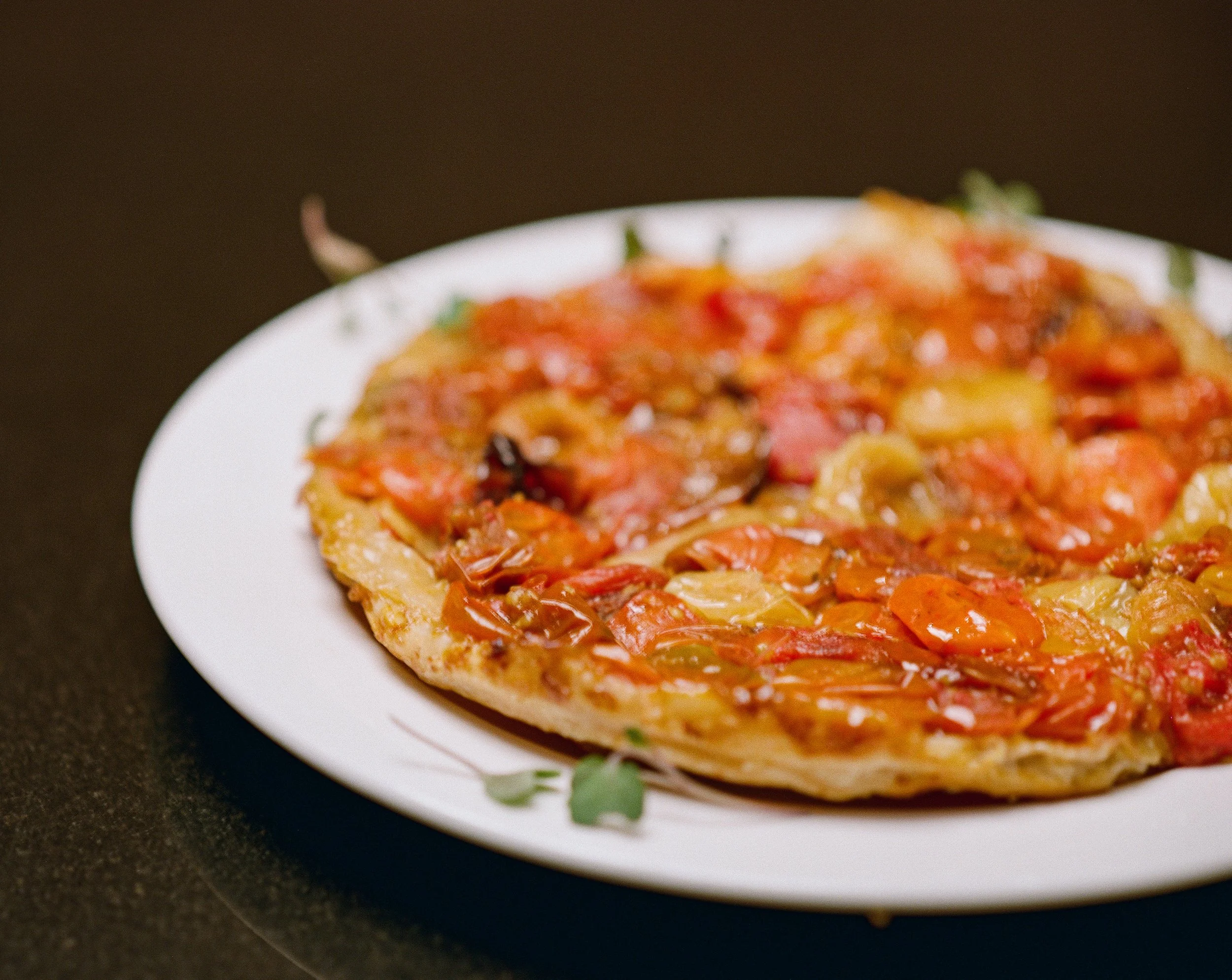 A pizza with various toppings on a white plate, placed on a dark surface.