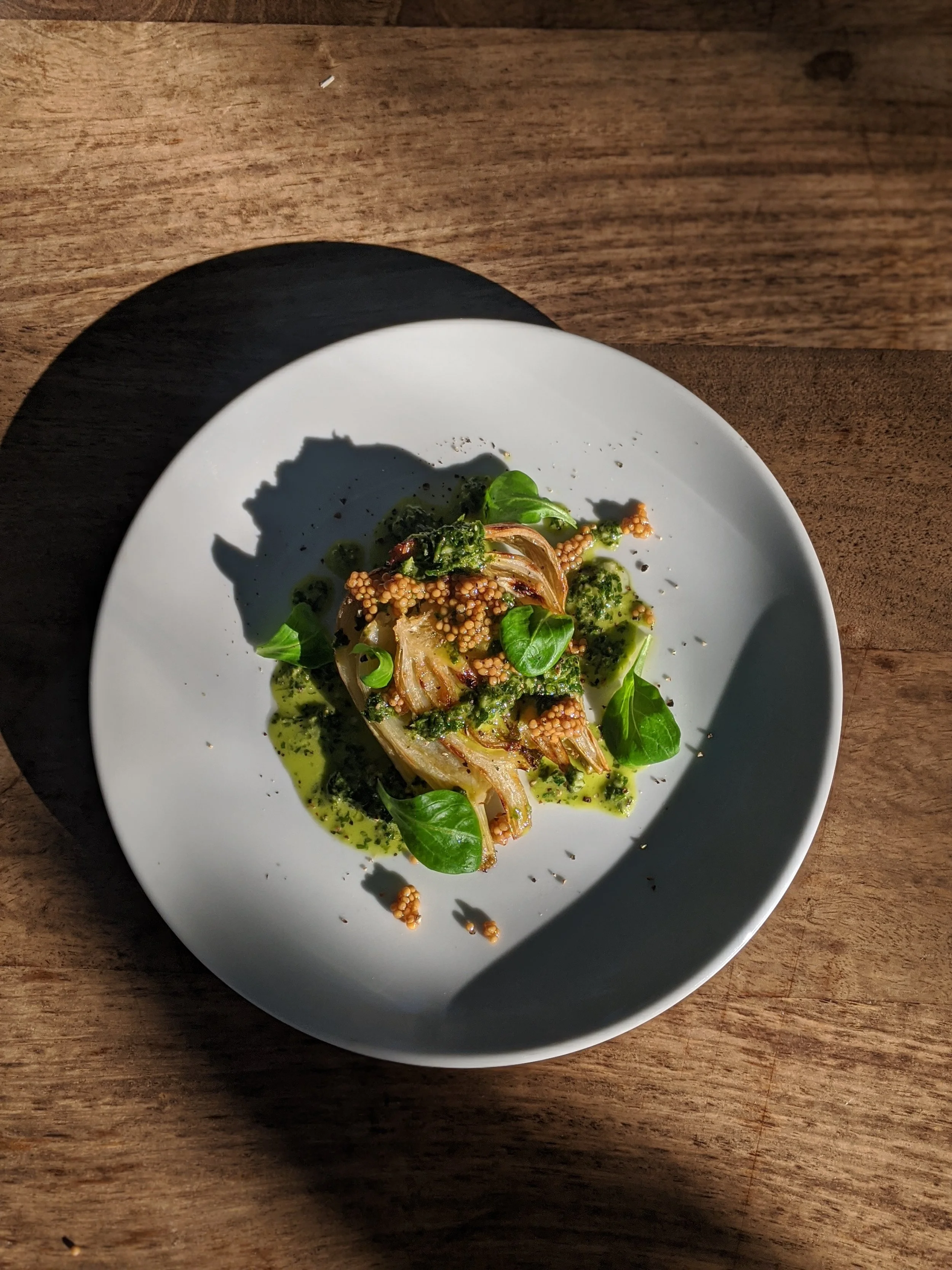 Gourmet dish with grilled vegetables, green sauce, mustard seeds, and fresh herbs on a white plate