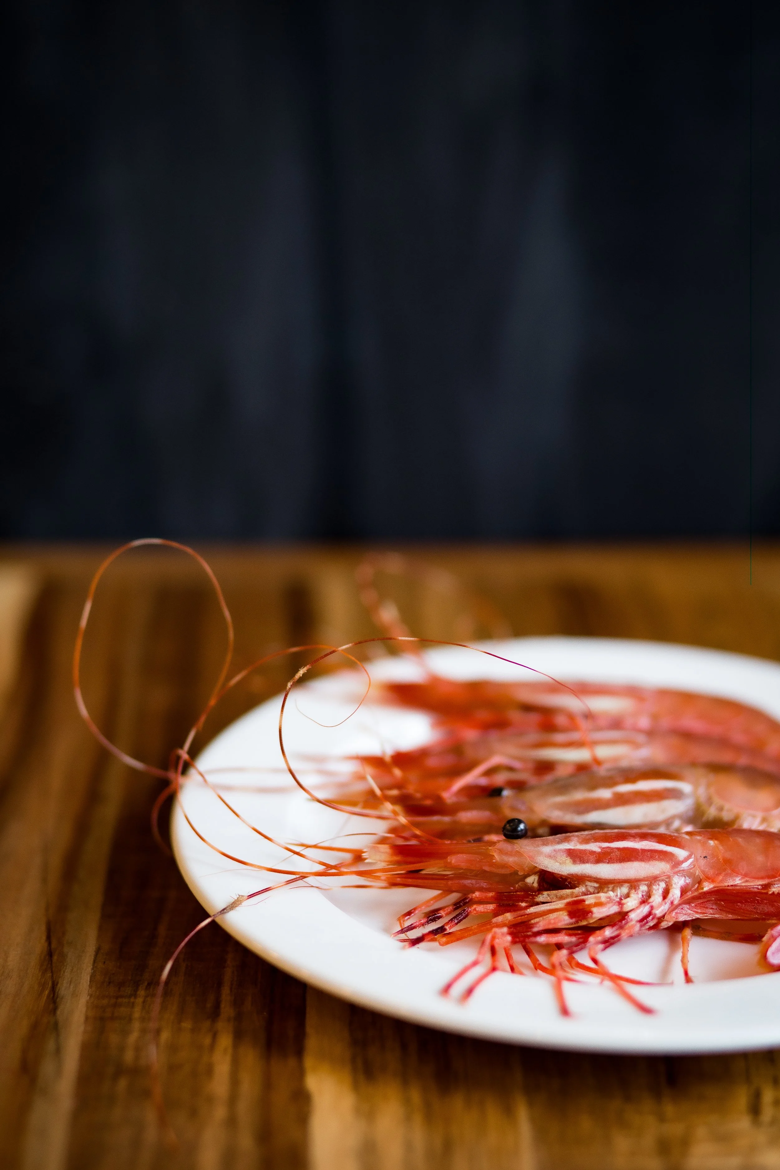 Fresh raw shrimp on a white plate on a wooden surface.