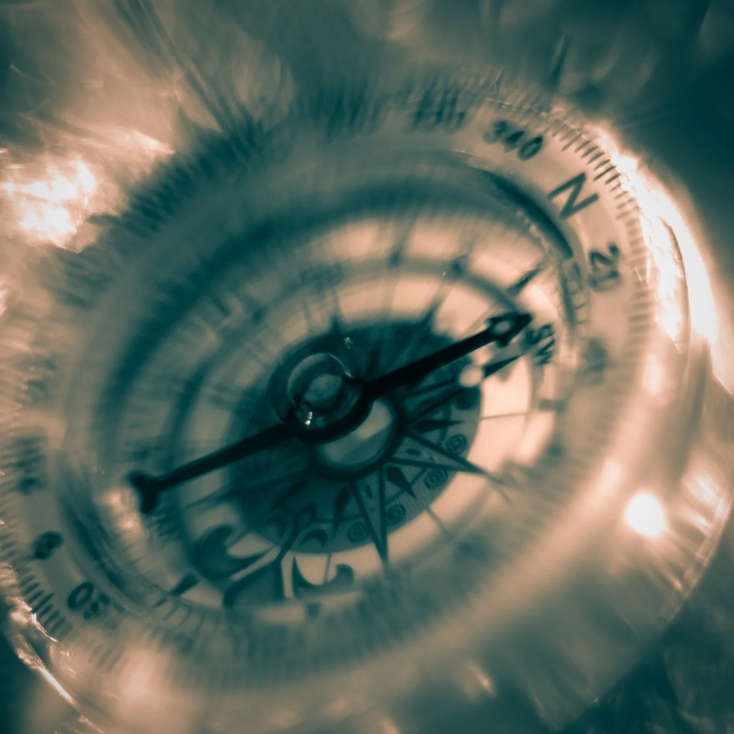 A compass photographed by Mark Robert Halper in teal and warm light.
