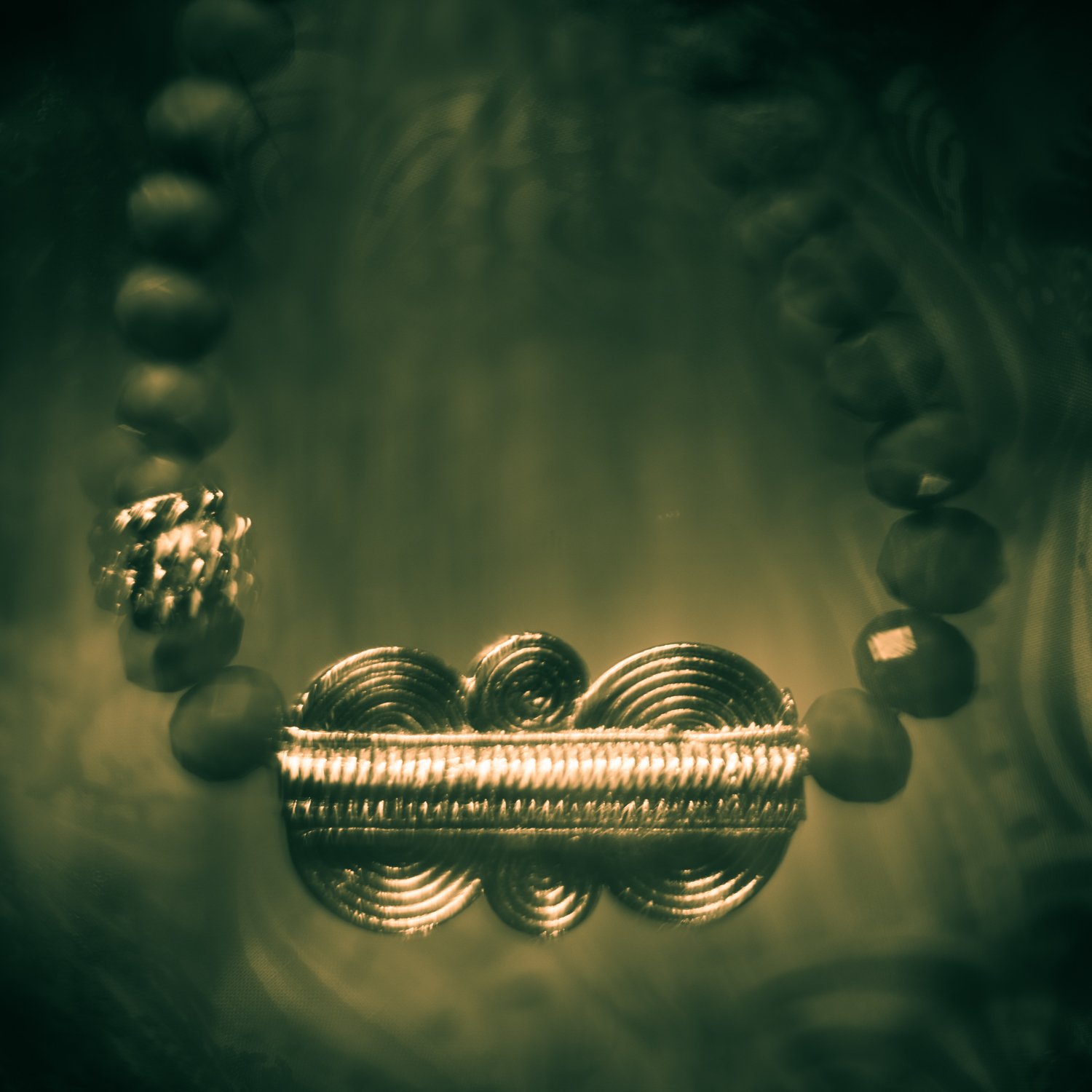 A necklace photographed by Mark Robert Halper in green and golden light.