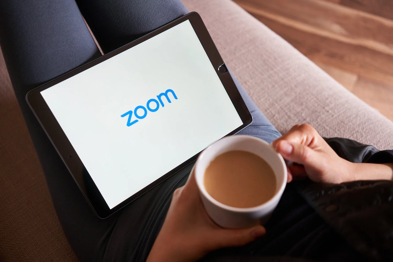 A person holding a cup of coffee looking at a computer tablet with the word Zoom on it to show webinars
