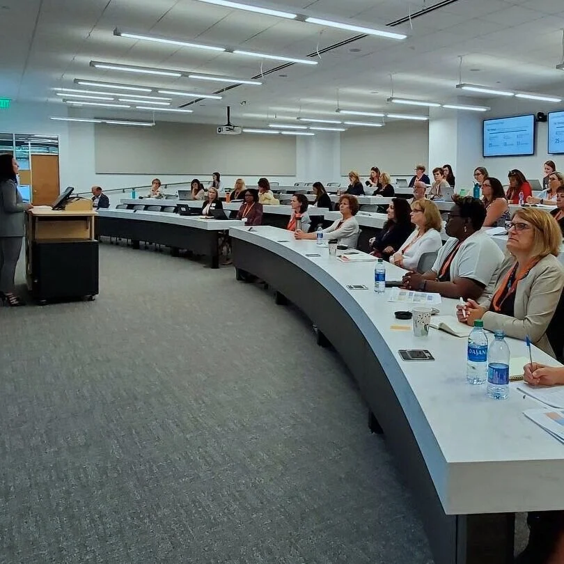 NIHD members sitting in a large conference room in a semi circle with a speaker in a class