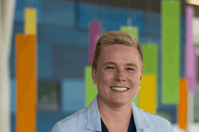 Smiling woman with short blonde hair and earrings in front of colorful bar graph background.
