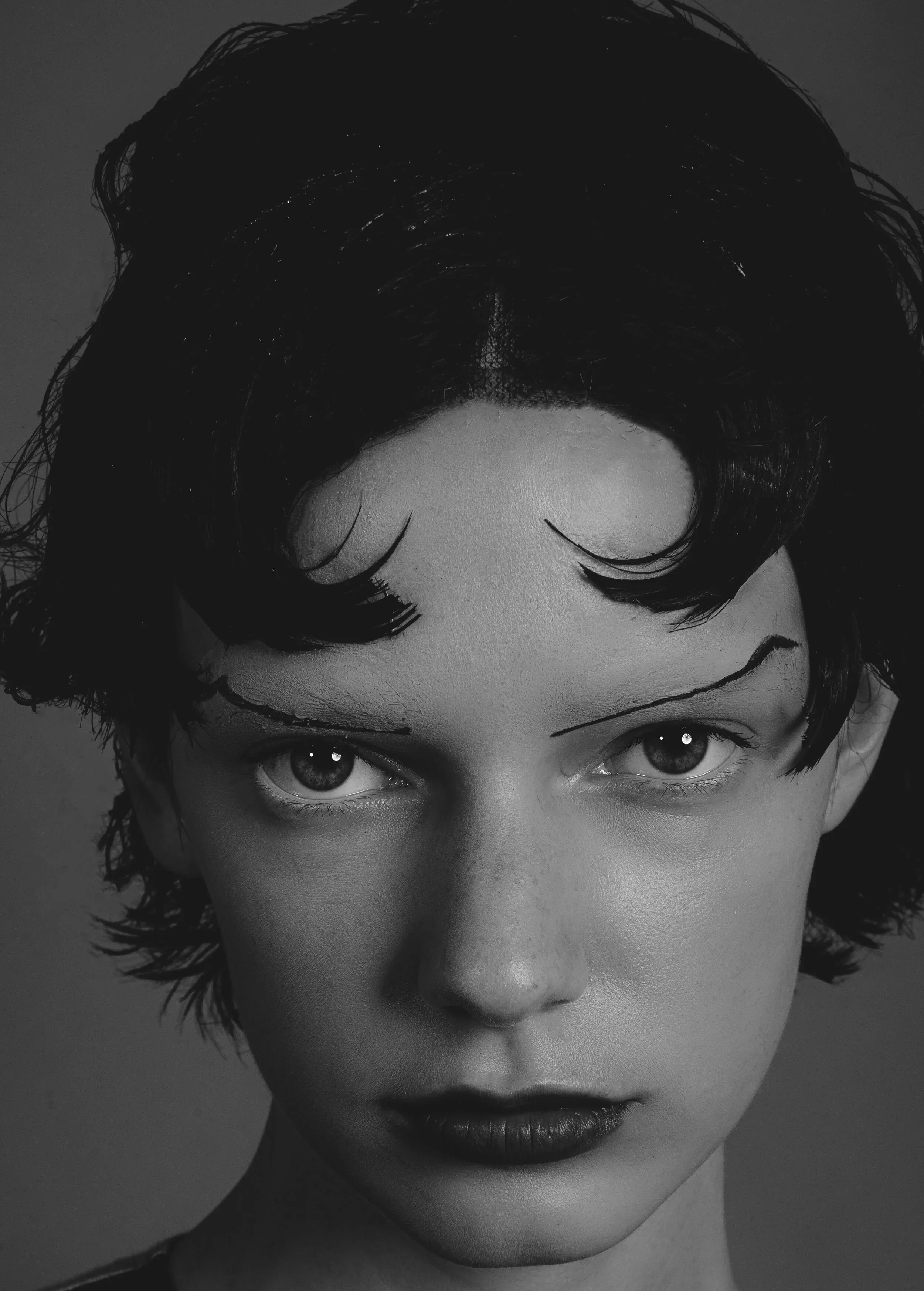 Retrato em preto e branco de uma mulher com sobrancelhas desenhadas, cabelo curto e mechas onduladas, com olhar direto e expressão séria.