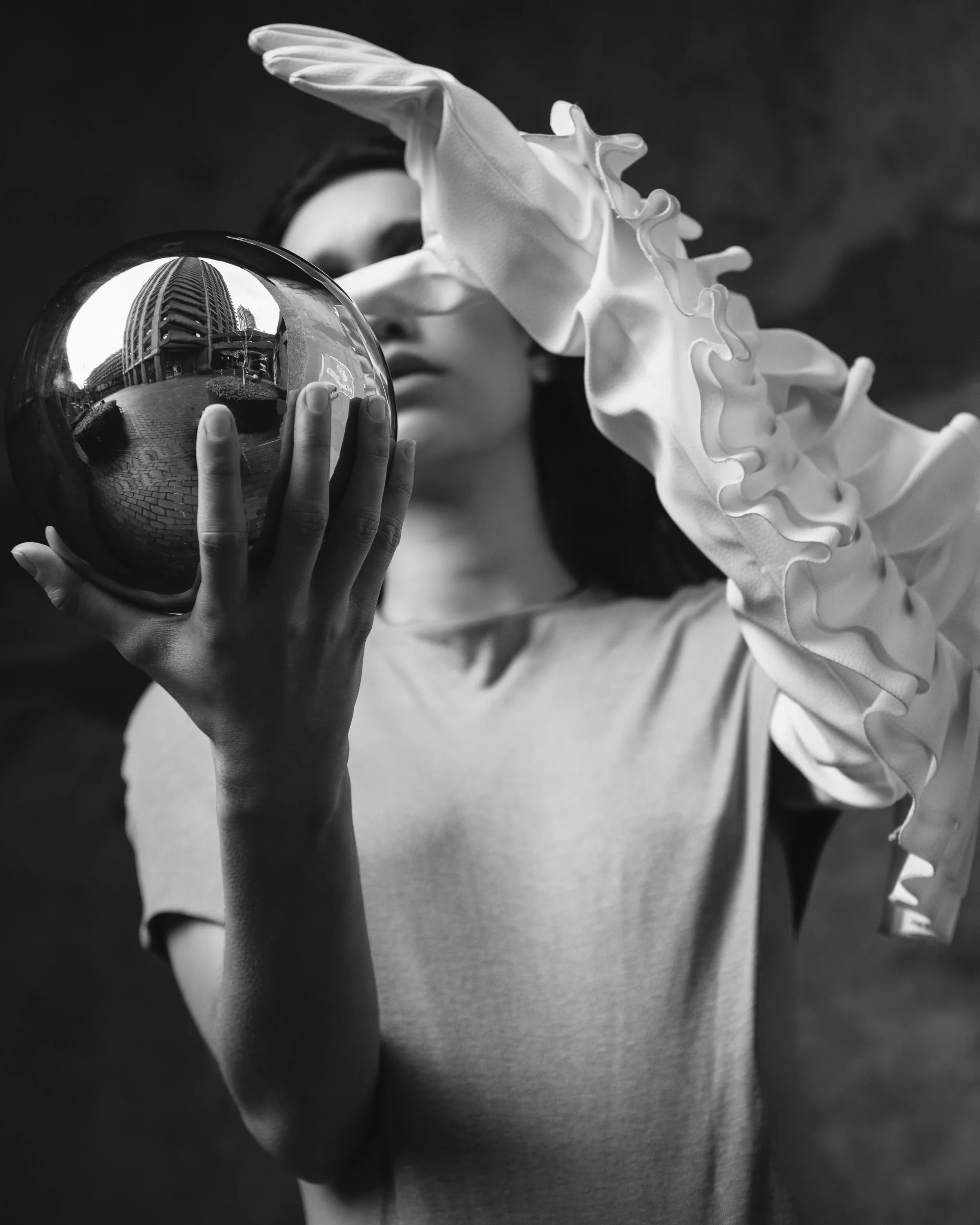 Pessoa com luvas brancas segurando uma bola espelhada, refletindo um edifício urbano.