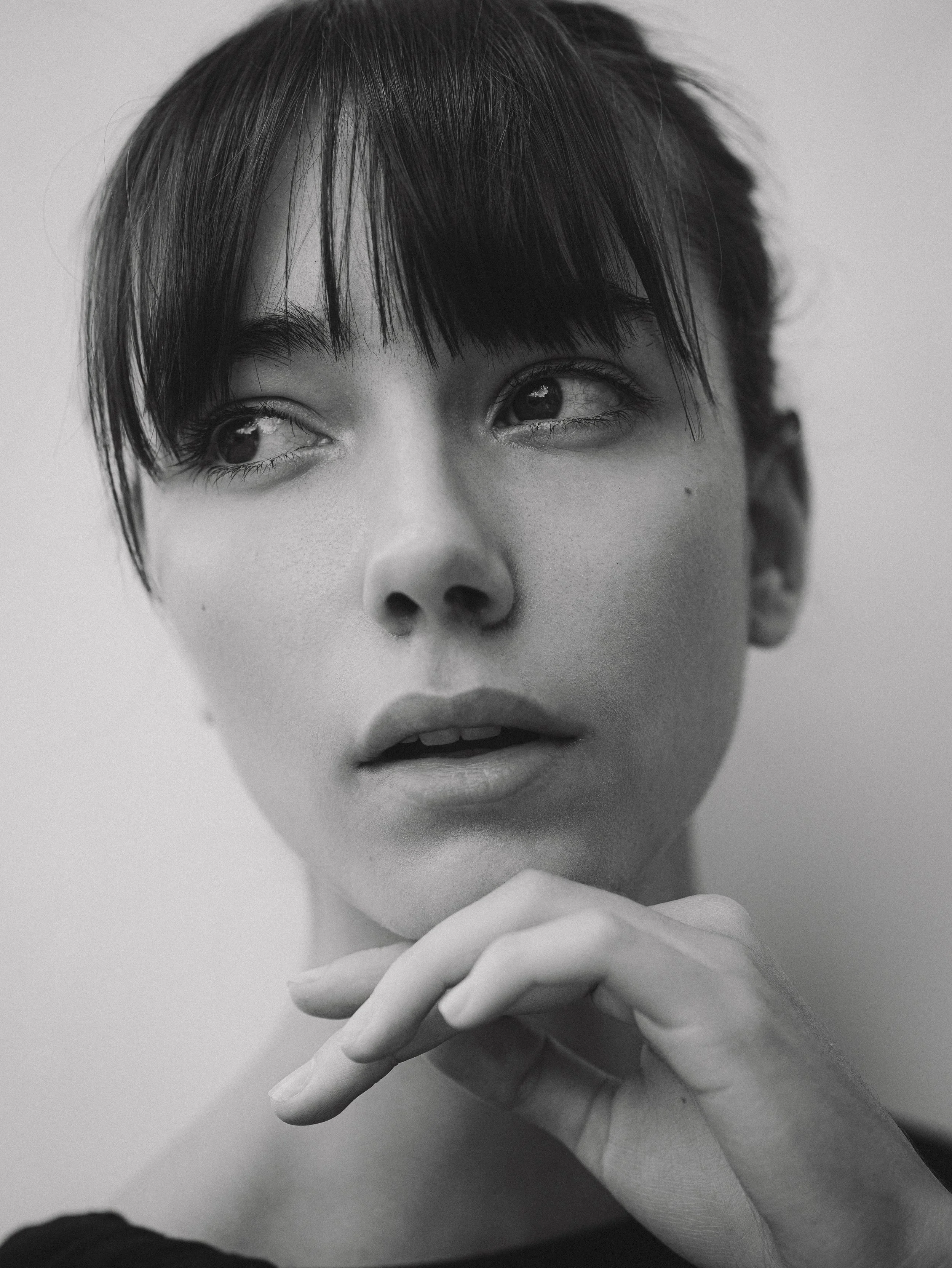 Retrato de uma mulher com cabelo curto e escuro, olhando para o lado, com expressão pensativa. Em tons de preto e branco.