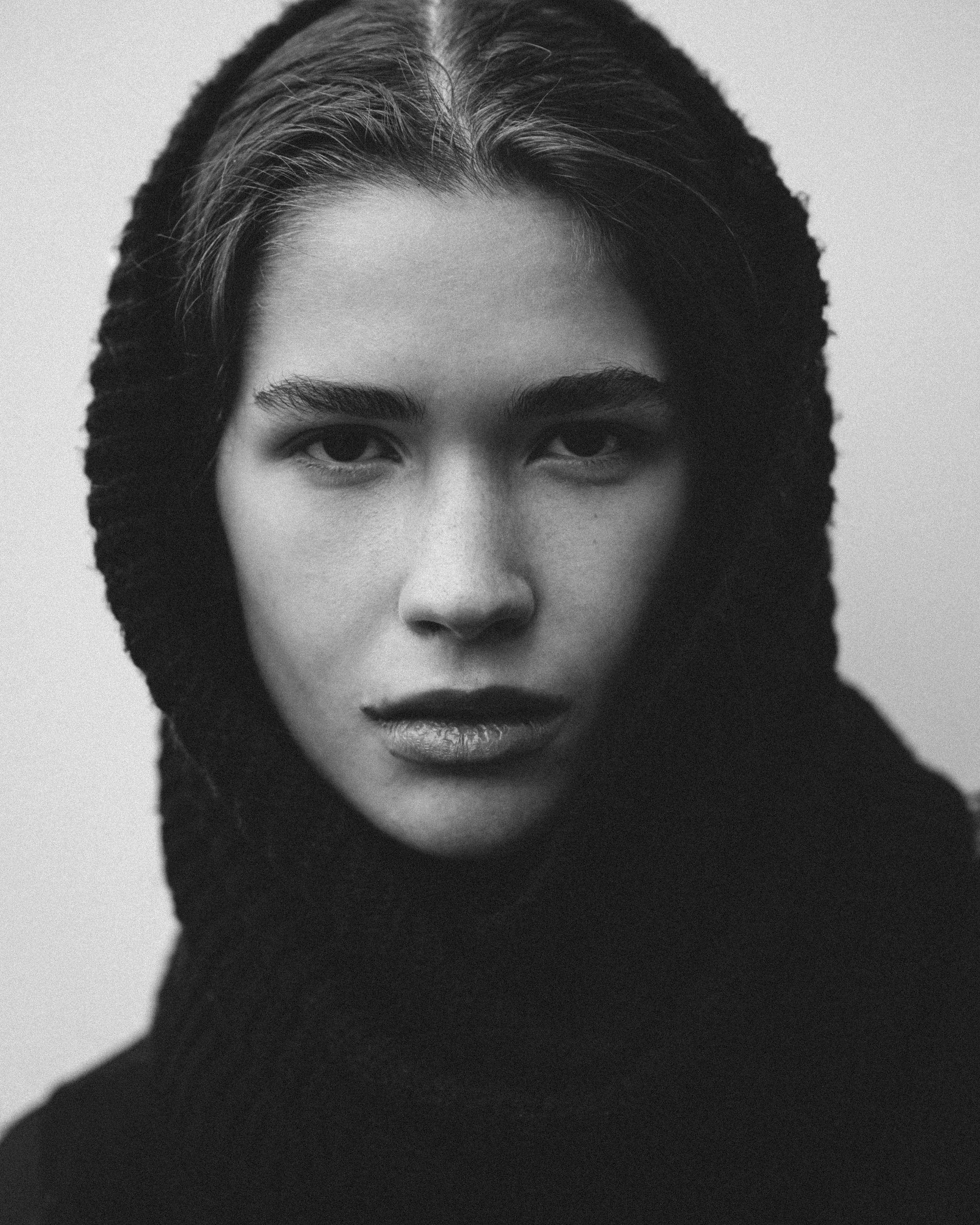 Retrato em preto e branco de uma mulher com cabelo escuro e penteado para trás, vestindo um suéter preto, olhando diretamente para a câmera.