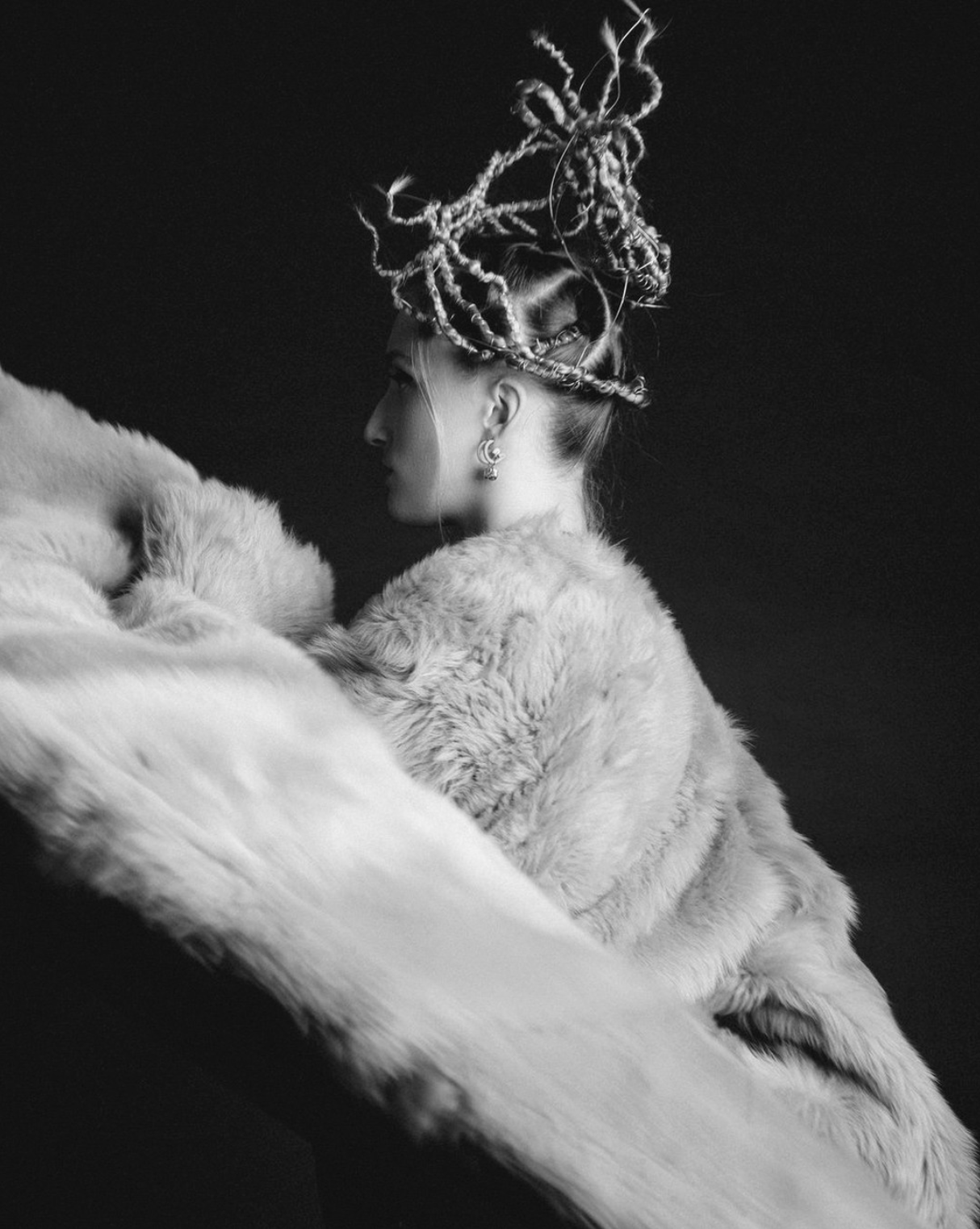 Retrato de uma mulher de perfil com penteado elaborado e cabelos encaracolados presos em um coque alto, vestindo uma roupa de pele em cores claras, contra um fundo escuro.