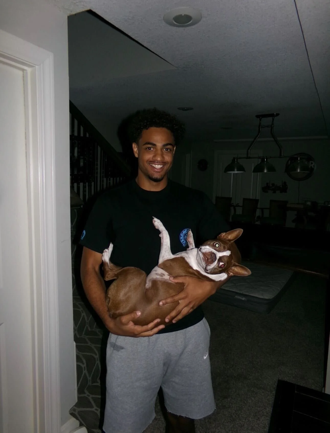 A young man holding a brown and white dog indoors in a living room.