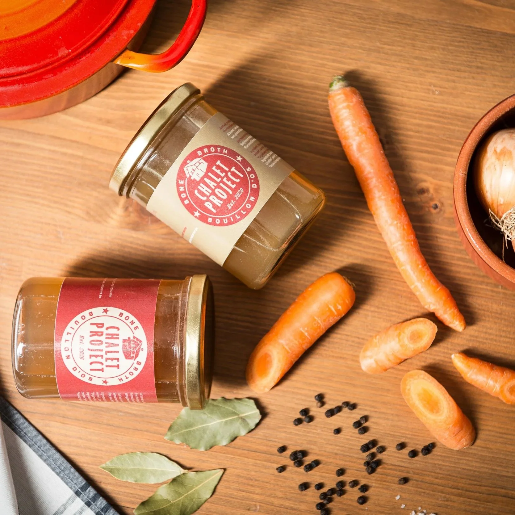 Deux pots de bouillon d'os avec étiquettes 'Chalet Project', avec légumes et assaisonnement.
