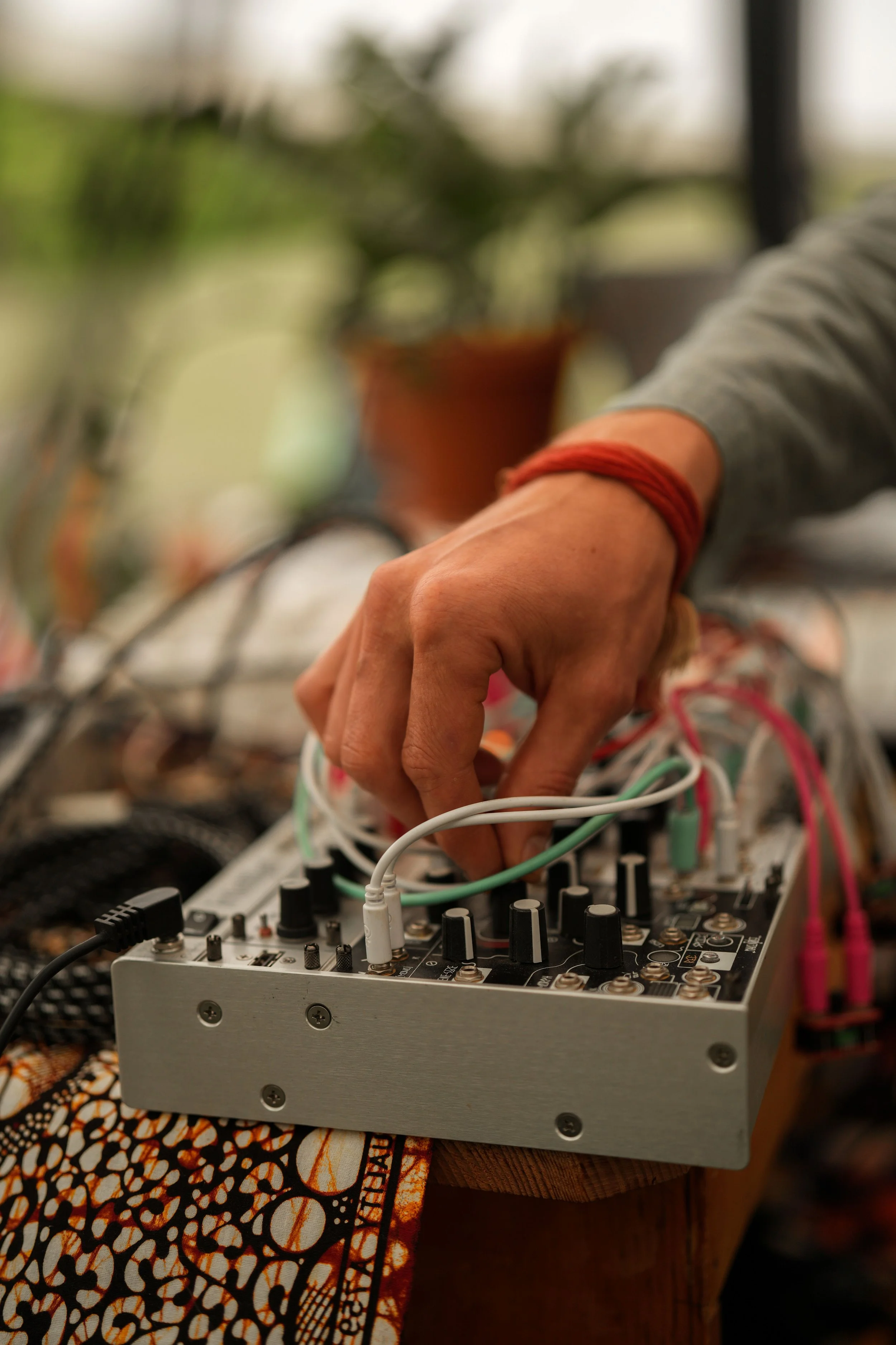 Close-up of a person's hand adjusting knobs on an electronic music synthesizer with multiple colorful cables connected.