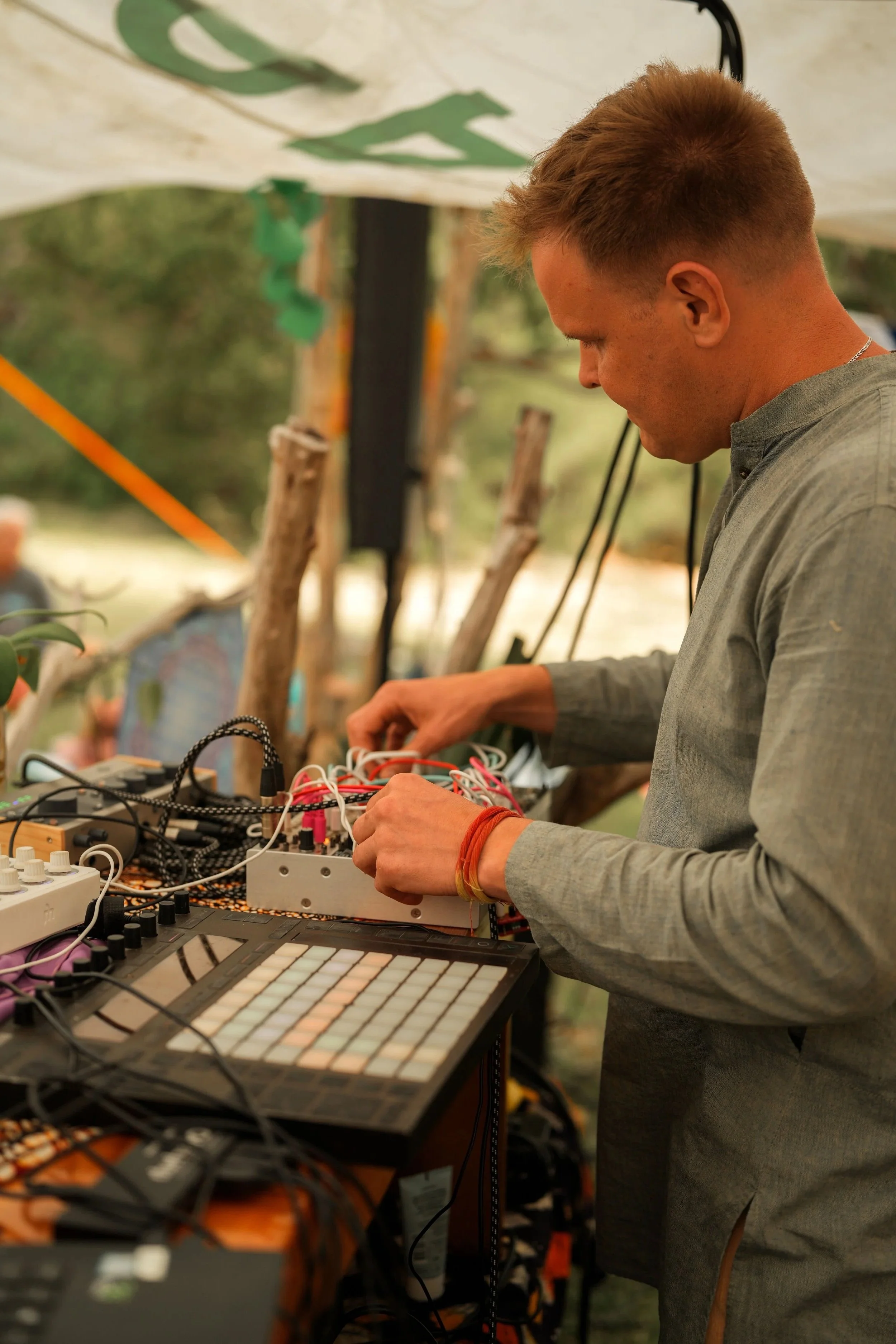 A man operating electronic music equipment outdoors under a canopy.