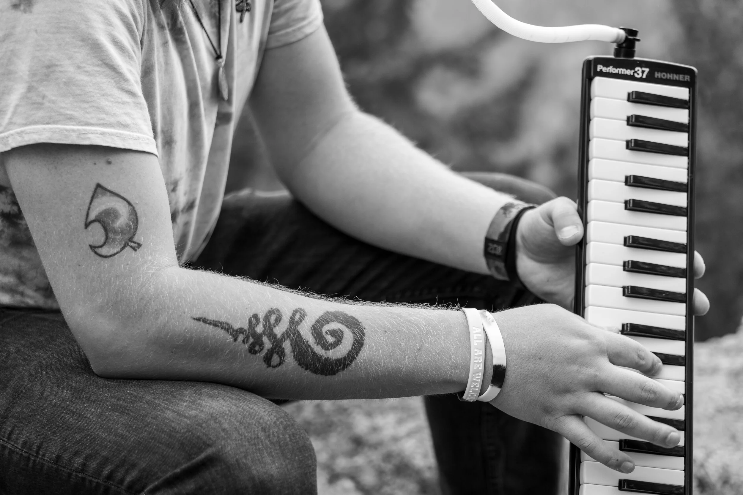 Person with tattoos on arm playing a small electronic keyboard outdoors.