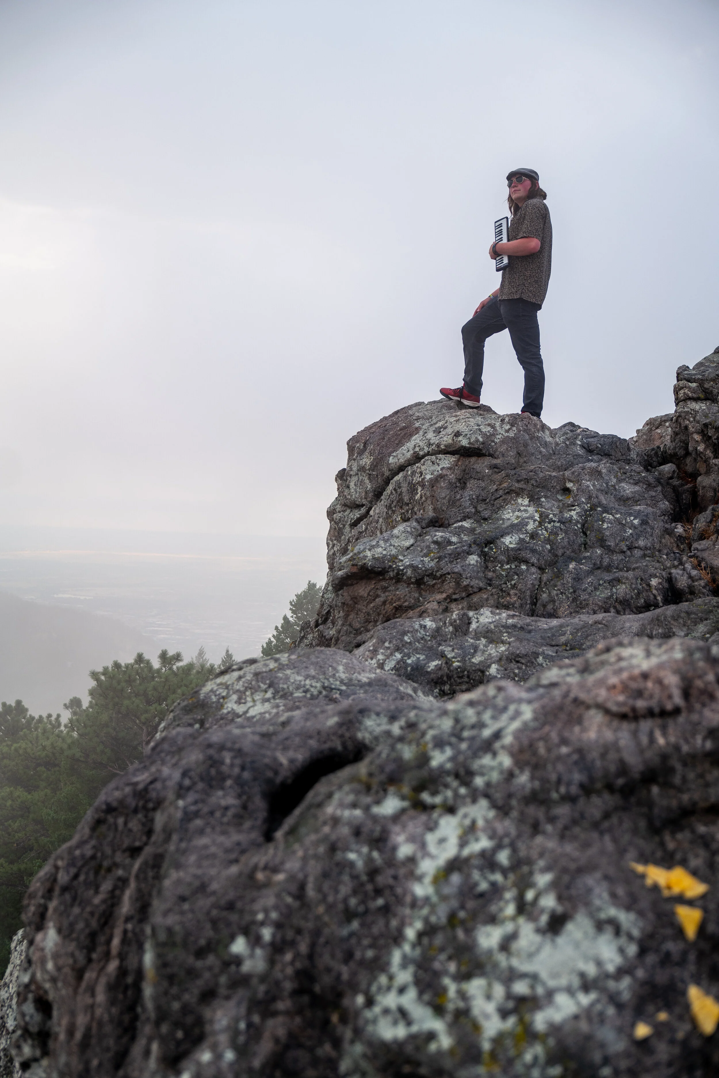Person standing on a large rocky outcrop holding a keyboard, with cloudy sky and trees in the background.