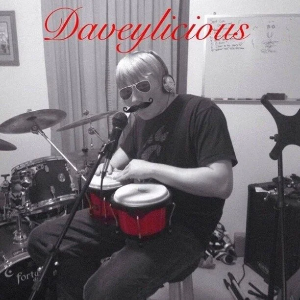 Person in a music studio with drums, wearing sunglasses and headphones, singing into a microphone, with added sunglasses and mustache filters. The word 'Daveylocious' is written across the top in red cursive.