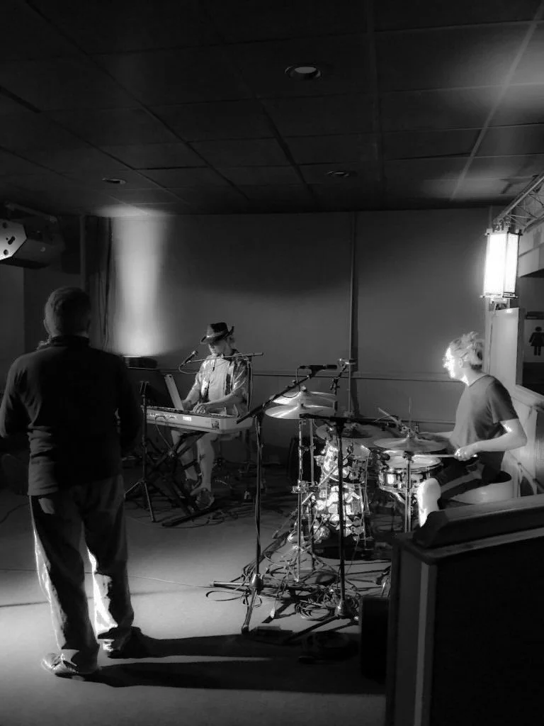 Two musicians rehearsing on a stage with a man standing in front of them, all in black and white.