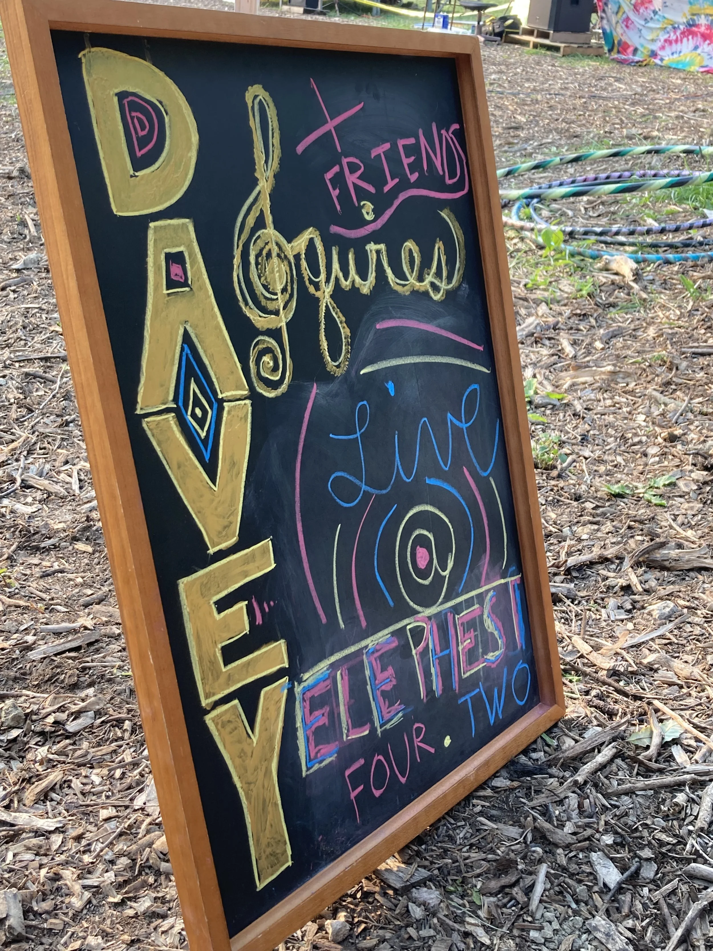 Colorful handwritten sign on a chalkboard advertising an event titled 'Love & Friends Quilts Live', scheduled for February 4th and 2nd, with decorative drawings and text.