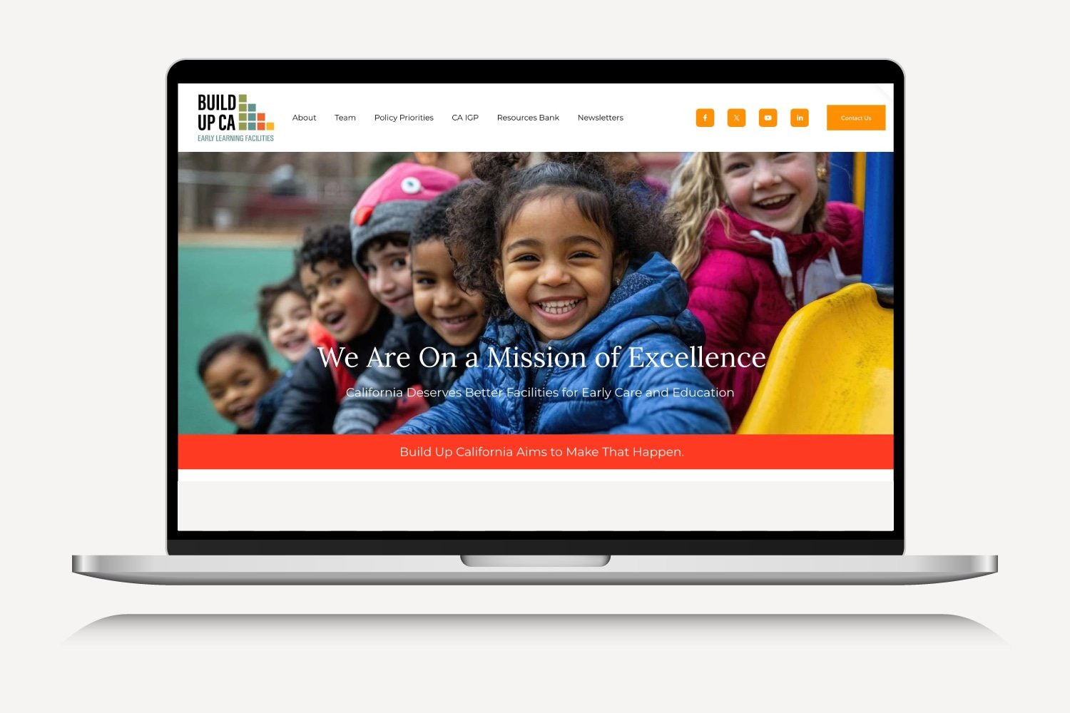 Laptop displaying an Education website with a photo of smiling young children playing outdoors, with a message about early education and community aims.