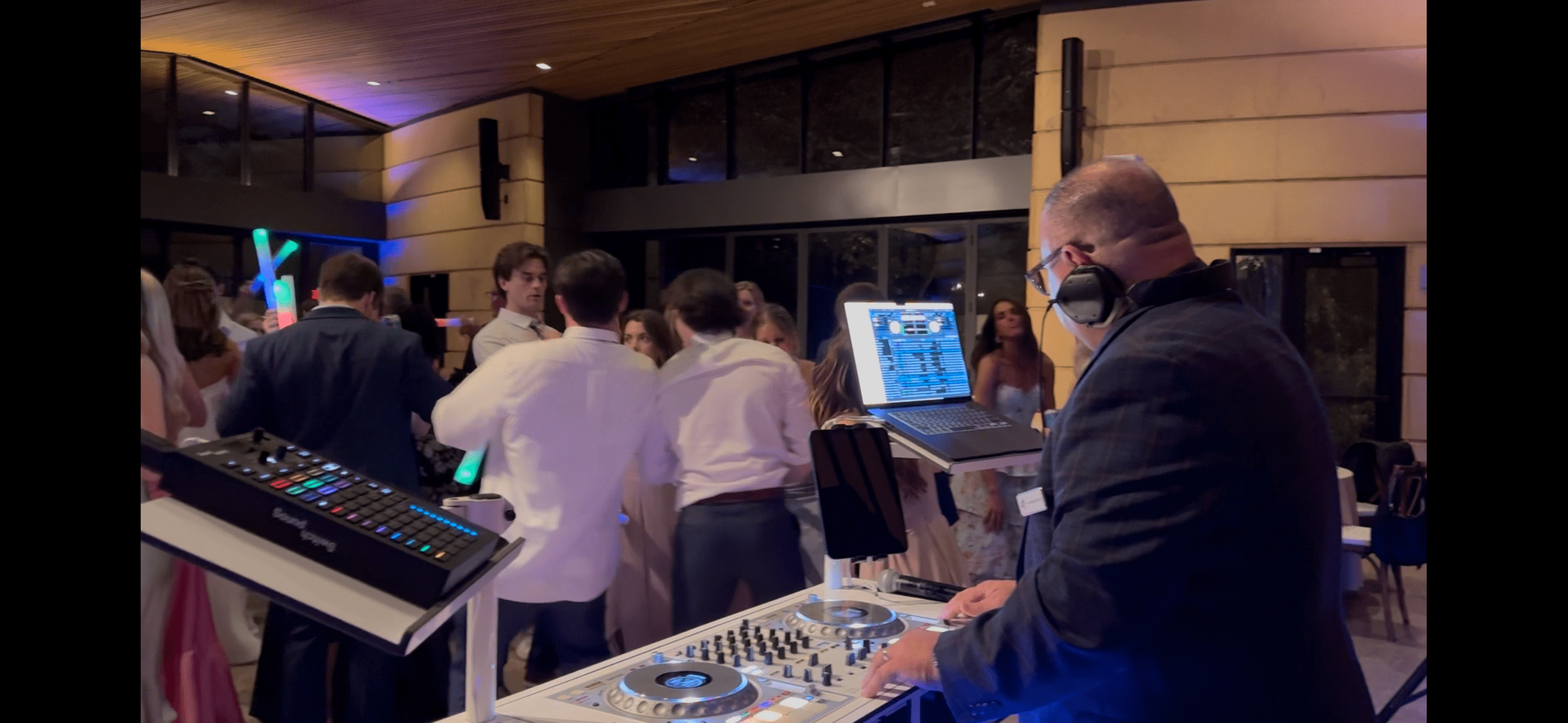 DJ performing with a laptop and sound equipment at a party with a crowd of people dancing.