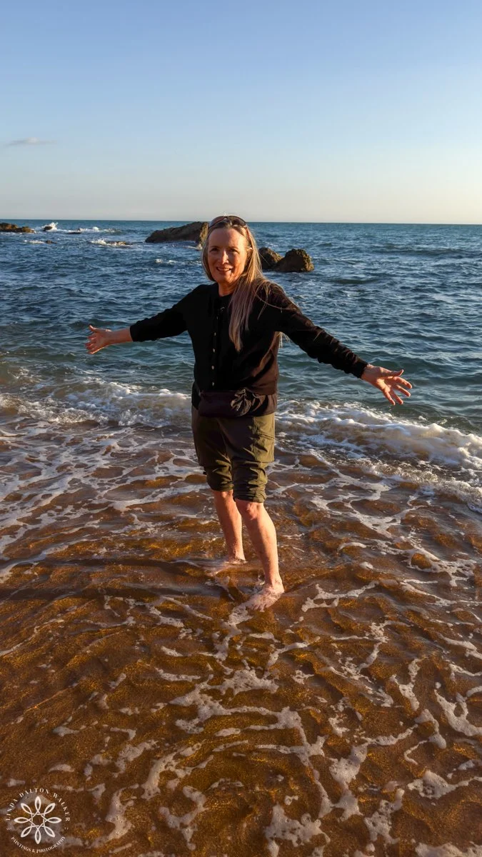 Author, photographer standing in cold water with arms outstretched, Sicily, Italy,