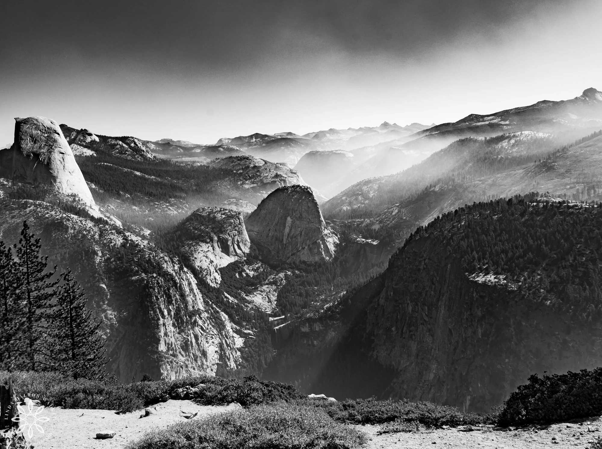 Black and white landscape photograph of layered granite cliffs and smoky haze over Yosemite Valley viewed from Glacier Point.