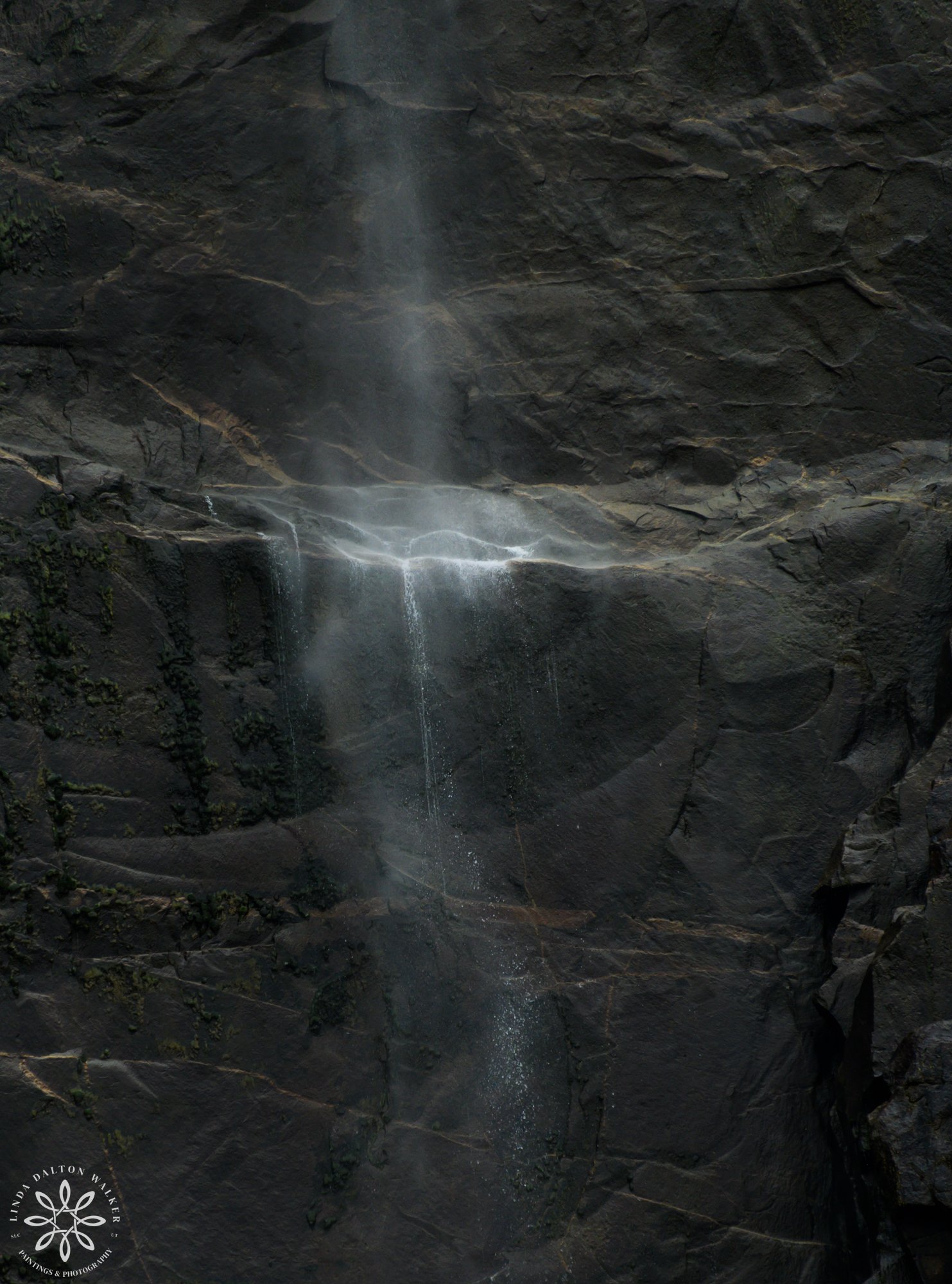 Close-up telephoto photograph of illuminated water mist hitting the dark granite rock face at Bridalveil Fall in Yosemite.
