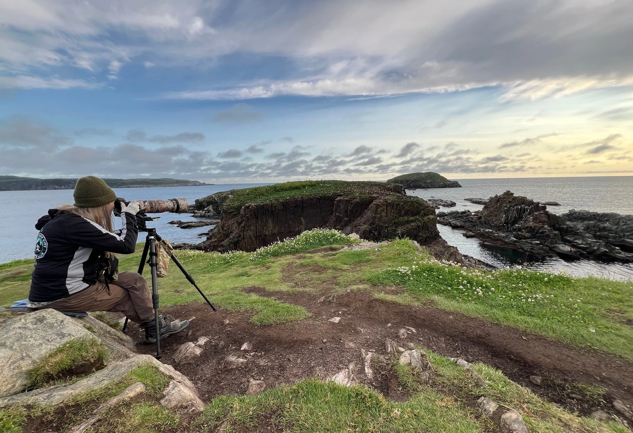 Female photographer sitting on a rock photographing to distance rocky rookery in Newfoundland