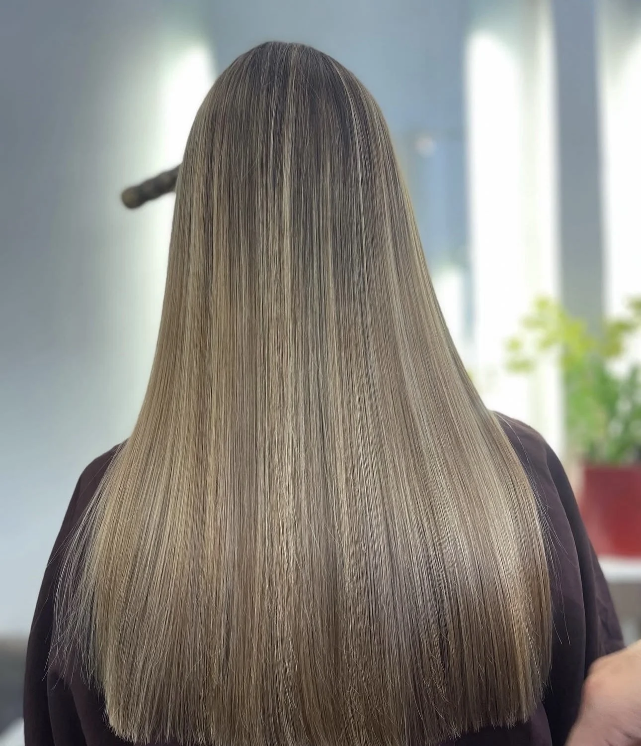 Back view of a woman with long, straight, blonde hair in a salon setting.