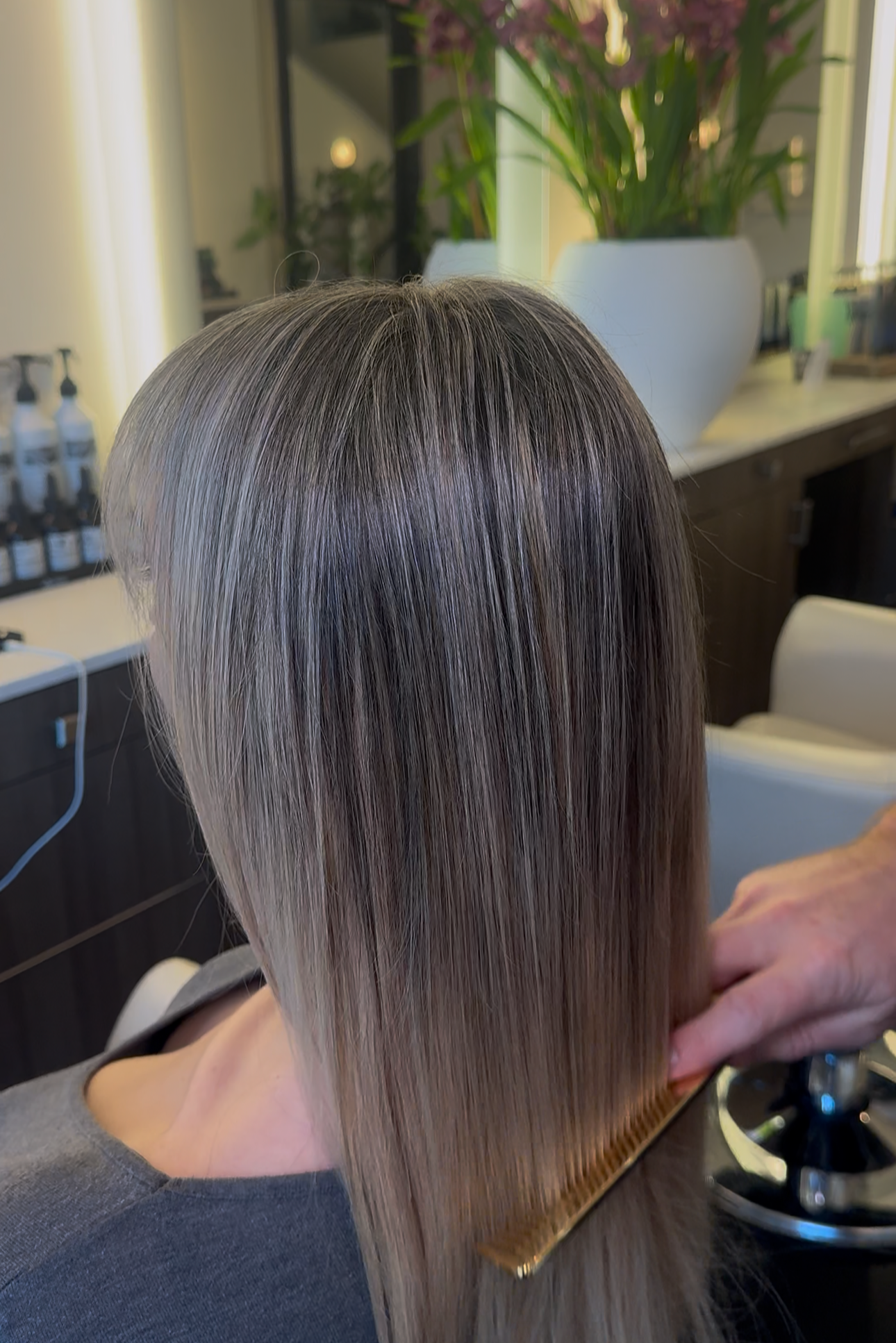 Person with straight, shiny, gray-blonde hair having their hair brushed at a salon.