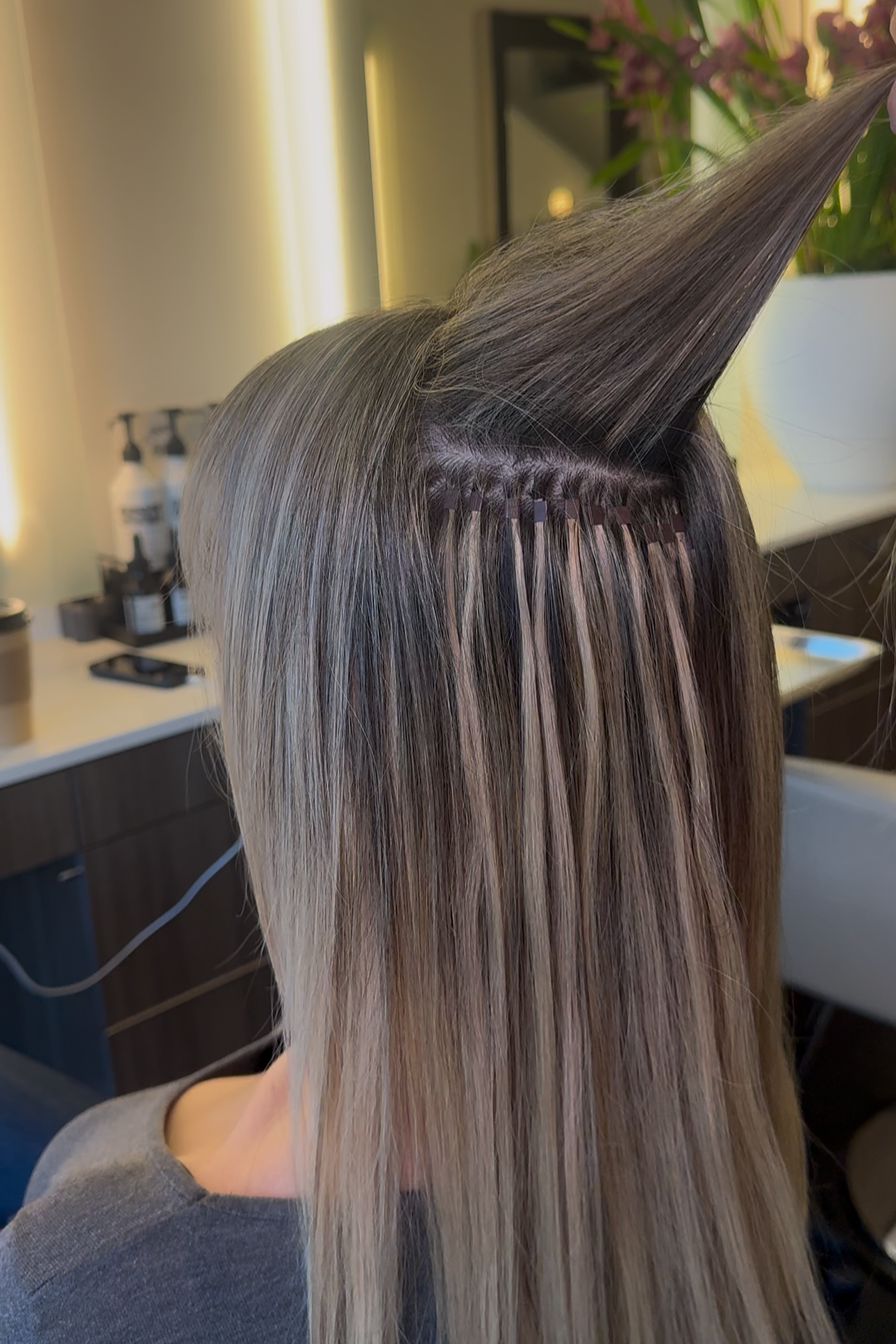 Close-up of a woman getting hair extensions or a hair treatment, with hair parted and sections secured, in a salon setting.