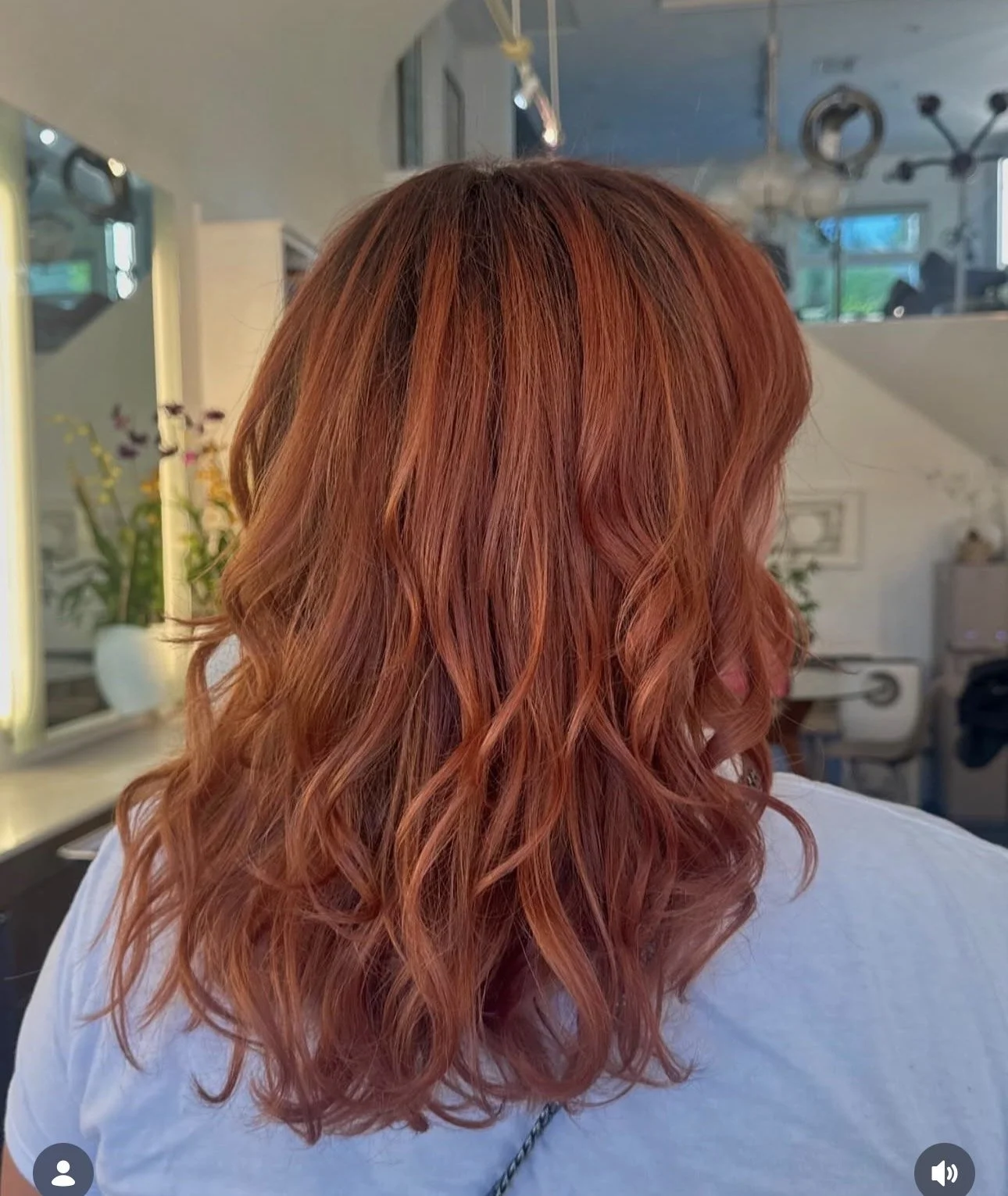 Back view of a woman with wavy, shoulder-length orange hair in a salon setting.