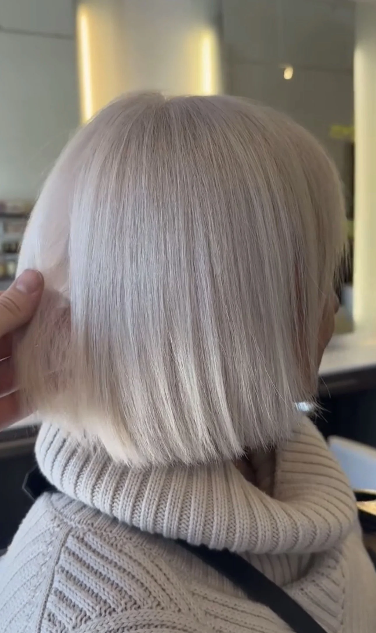 Close-up of blonde bob haircut on a person with a beige turtleneck.