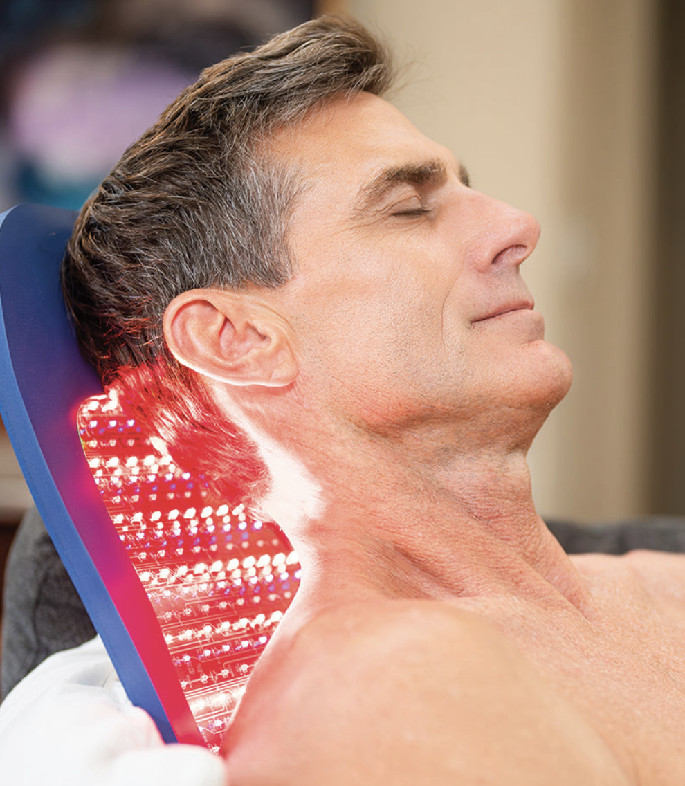 A man relaxing with his eyes closed, sitting in a reclined chair, with a digital laser therapy treatment being applied to the back of his neck.
