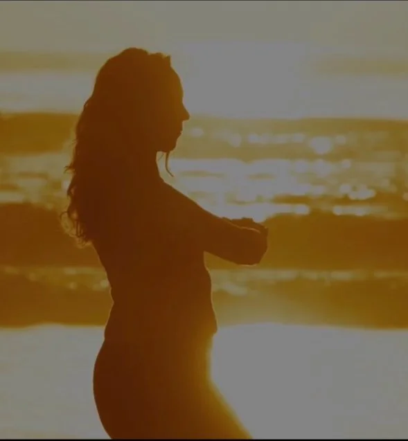Silhouette of a pregnant woman standing on the beach with arms crossed during a sunset.