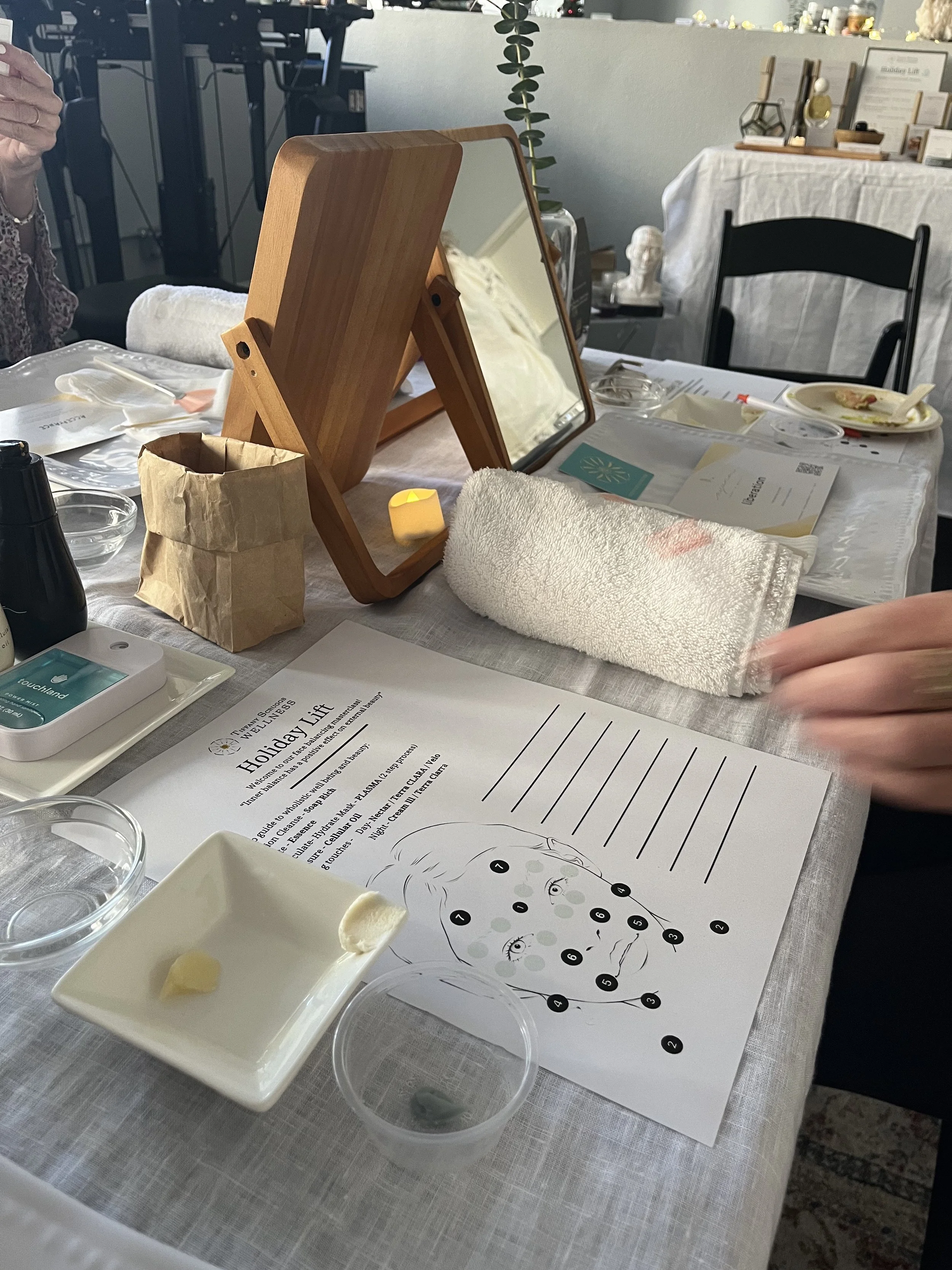 A table setup for a skincare or beauty treatment with a mirror, towels, small bowls, and skincare products. There is a diagram for a facial treatment, along with some papers and a tissue box.