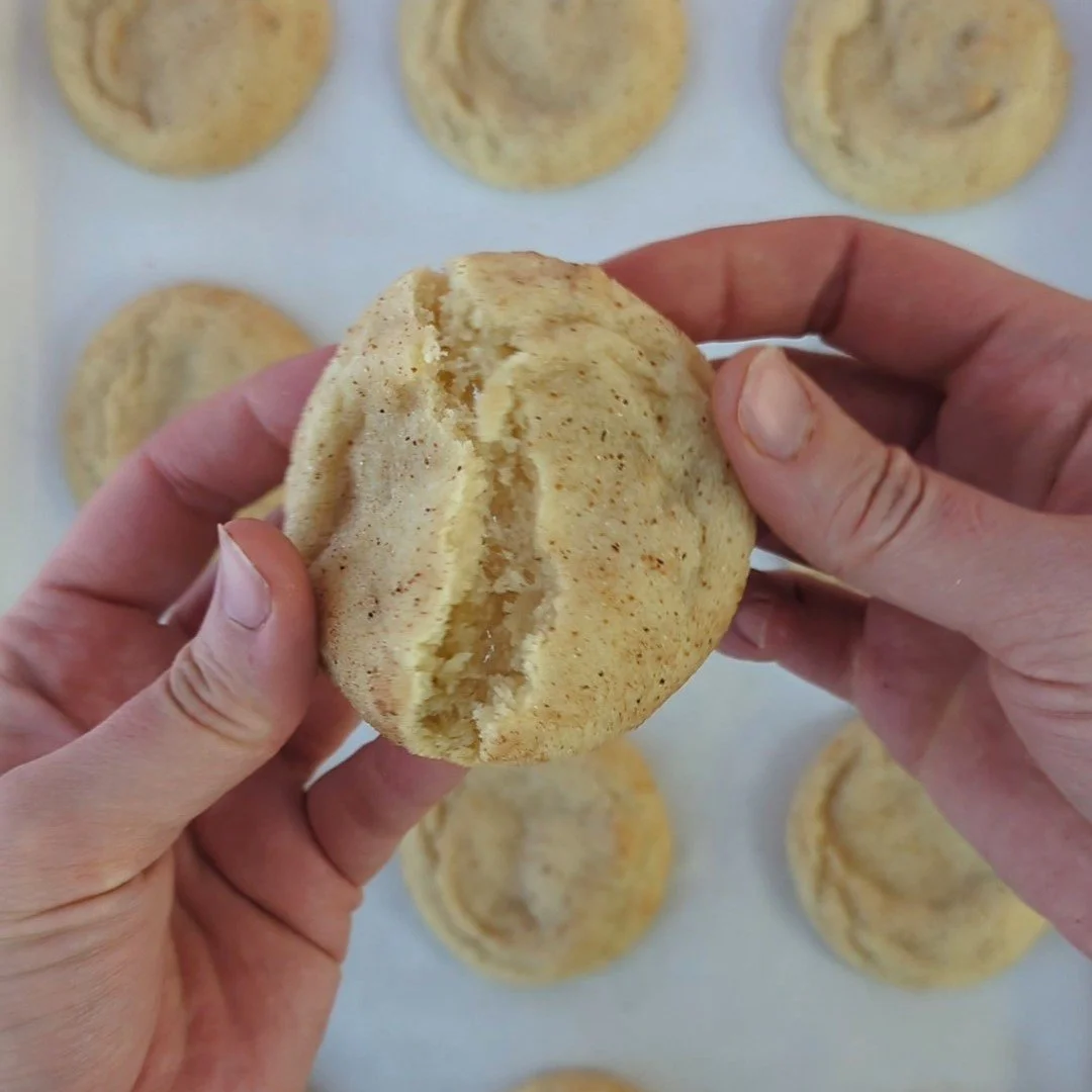 a close up of an eggnog spice cookie being broken in half. In the background you can see a full tray of cookies.